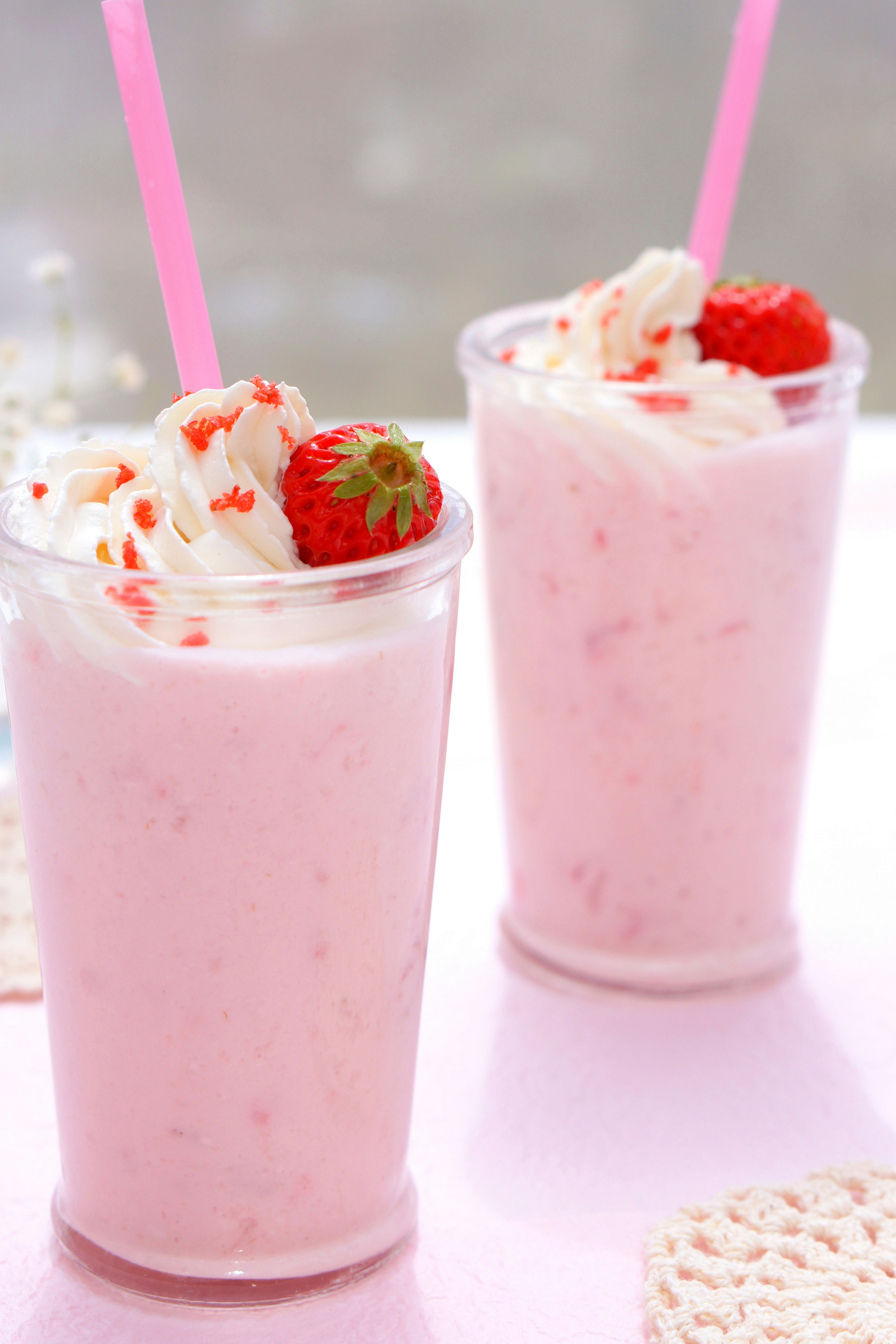 Due bicchieri di frappè alla fragola guarniti con panna montata e fragole