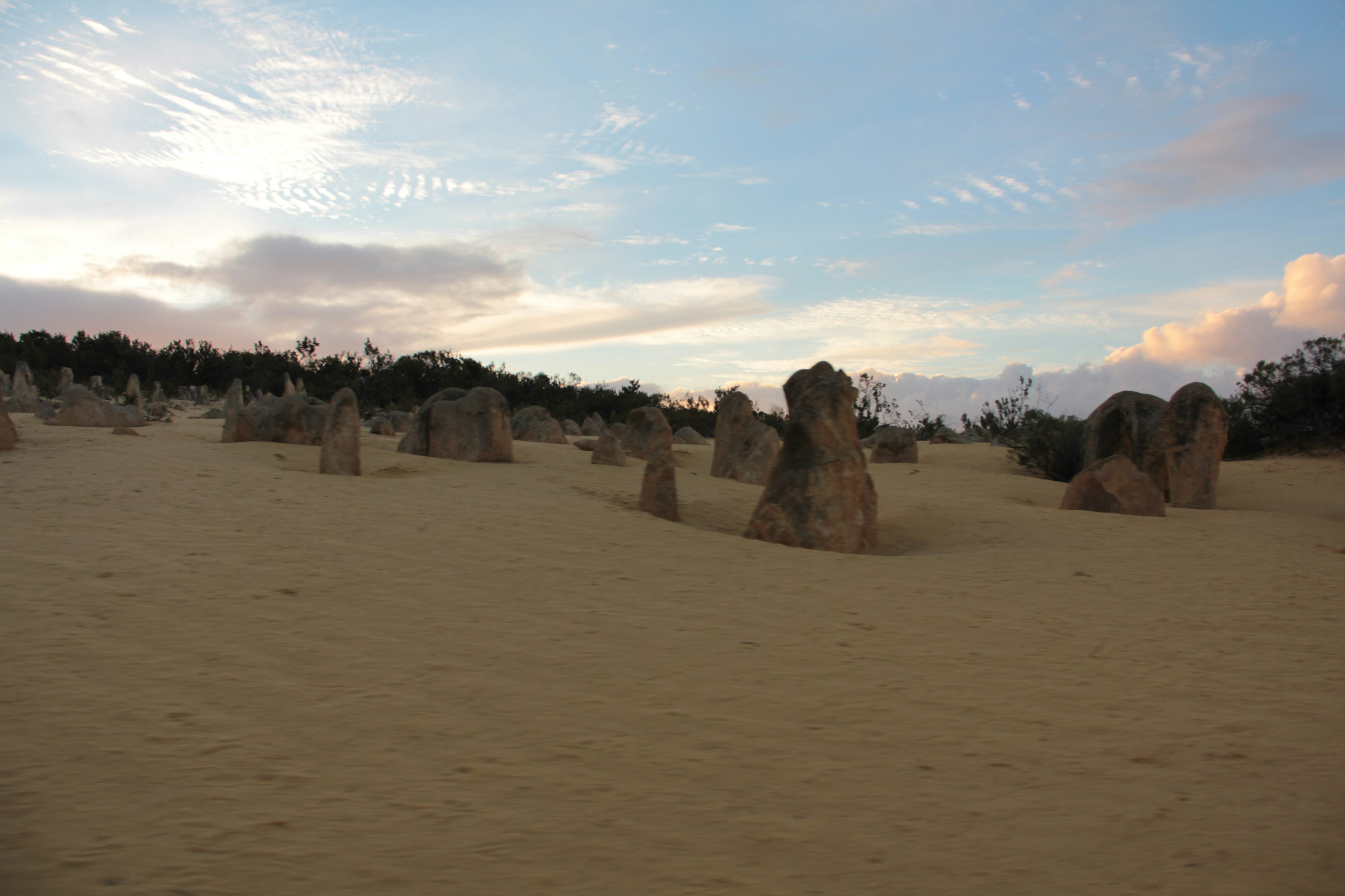 Large rock formations scattered across sand dunes under a blue sky