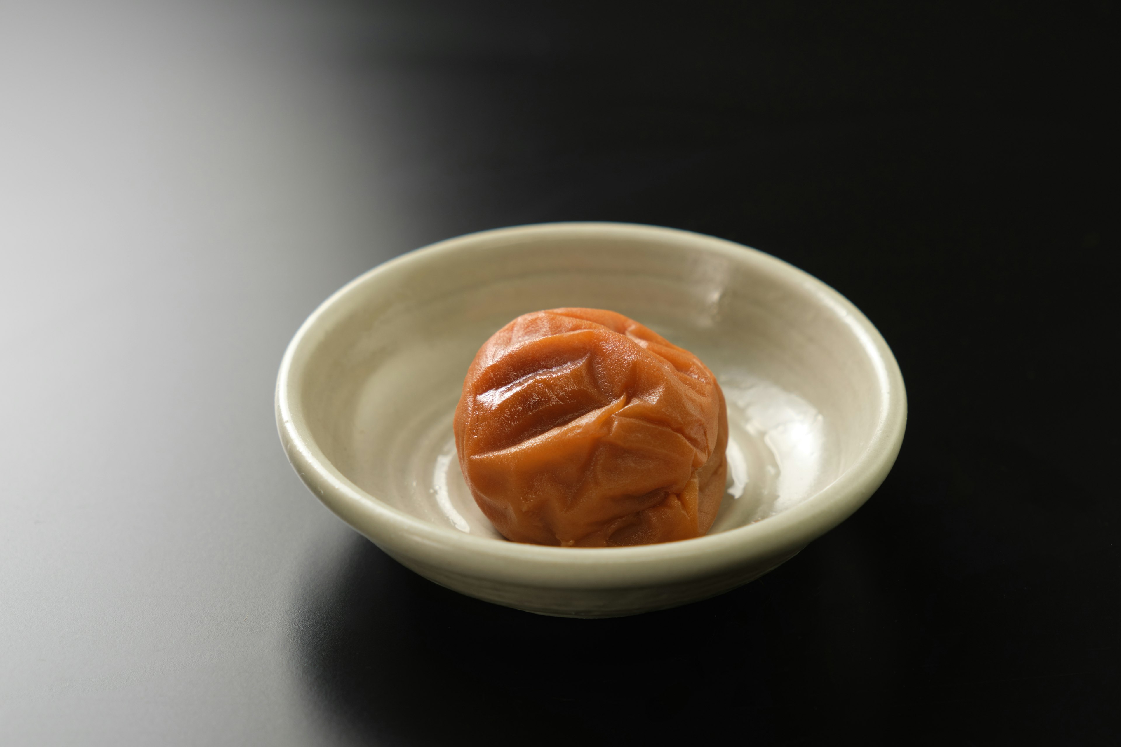 A umeboshi placed in a small white dish on a dark surface