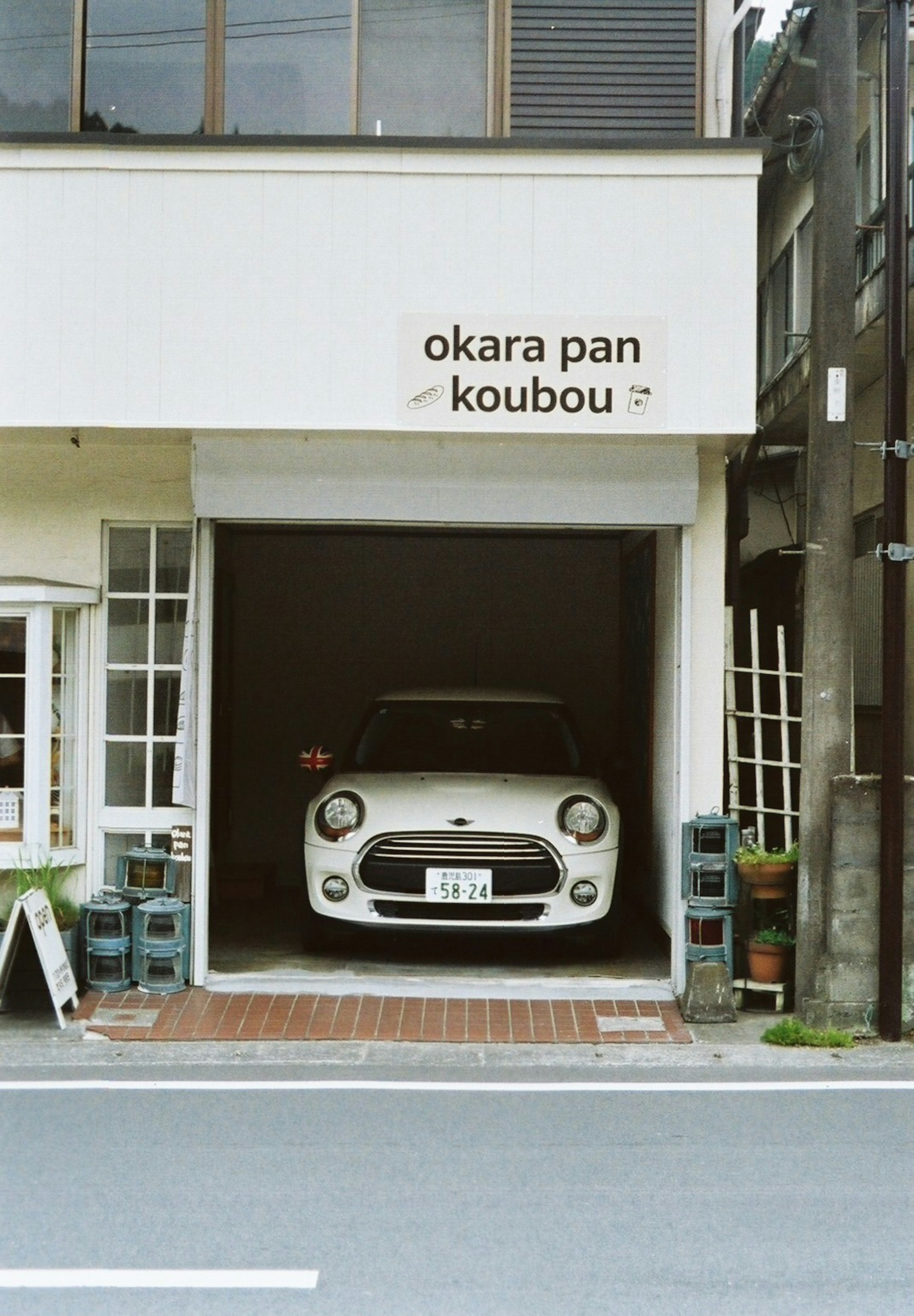 Un coche blanco estacionado en el garaje de una tienda con un cartel que dice okara pan koubou