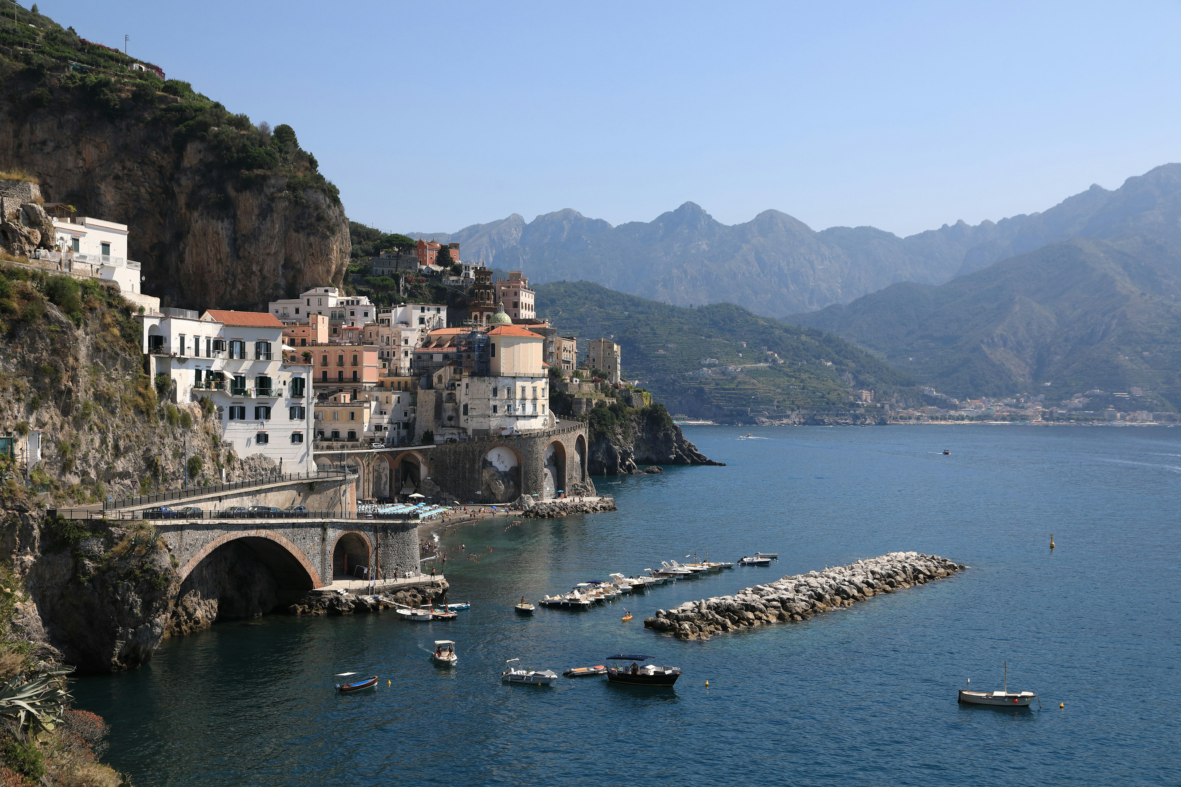 Villaggio costiero panoramico con montagne sullo sfondo e barche in acqua