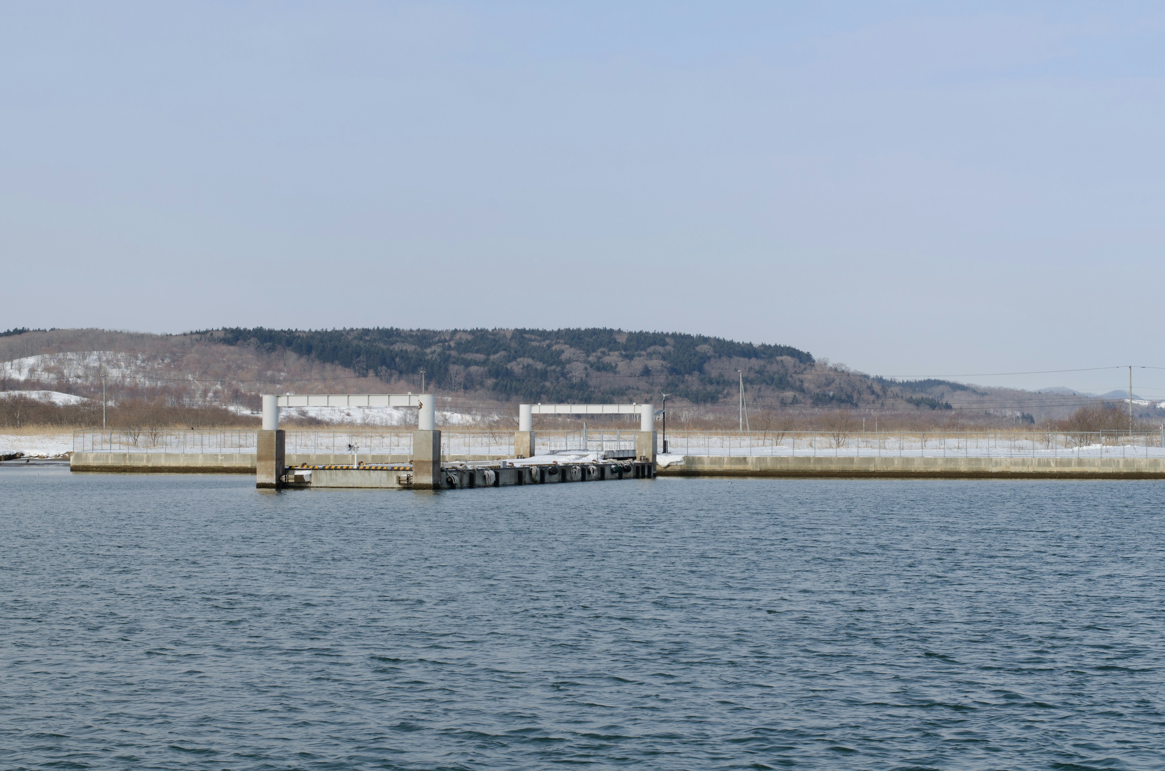 Dock extending into calm water with snow-covered hills in the background