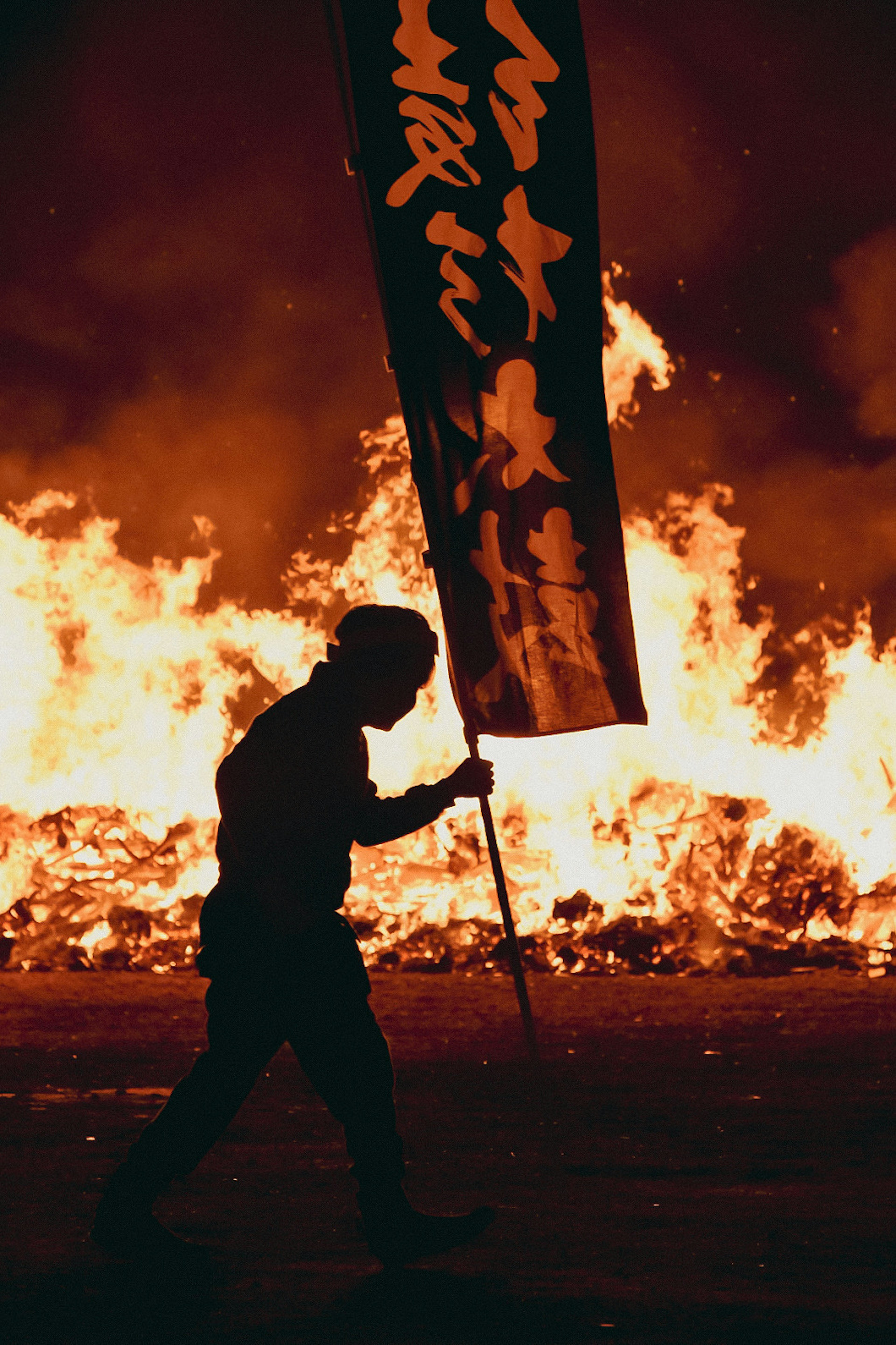 Silhouette d'une personne tenant un drapeau marchant devant des flammes