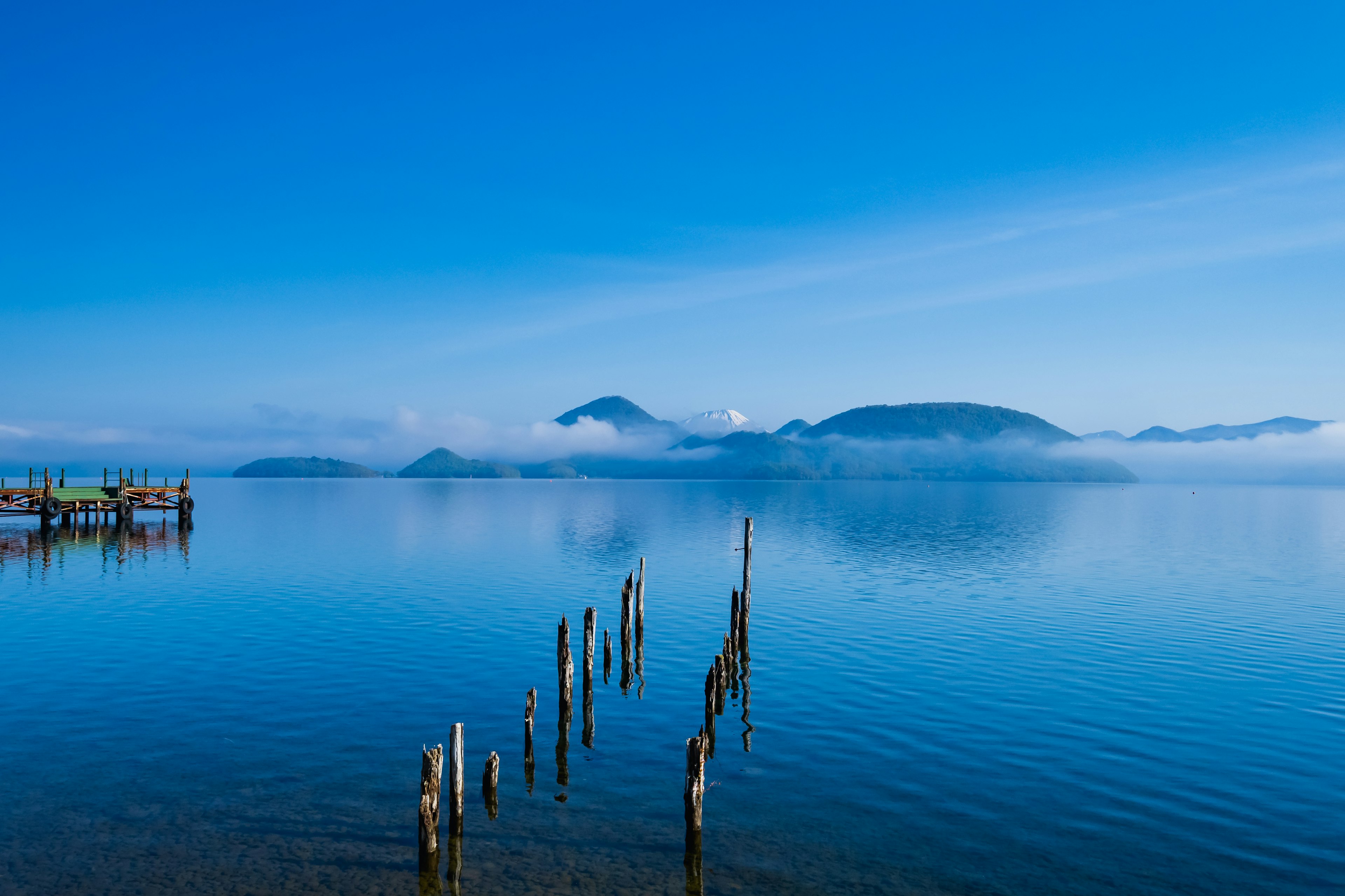 Vista panoramica di un lago blu con montagne nebbiose sullo sfondo pali vecchi nell'acqua