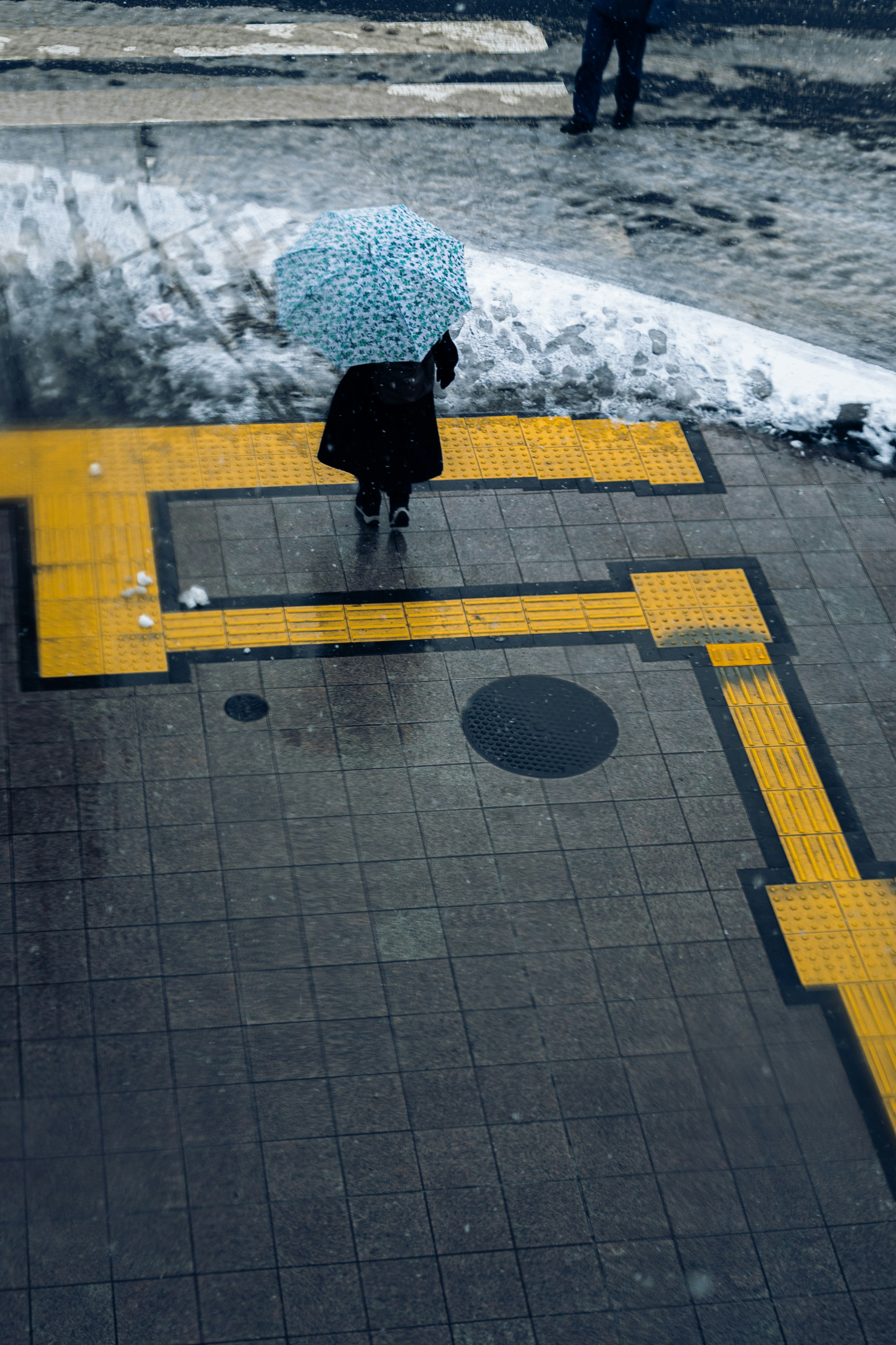 Une femme se tenant avec un parapluie bleu sur un pavé avec des lignes jaunes