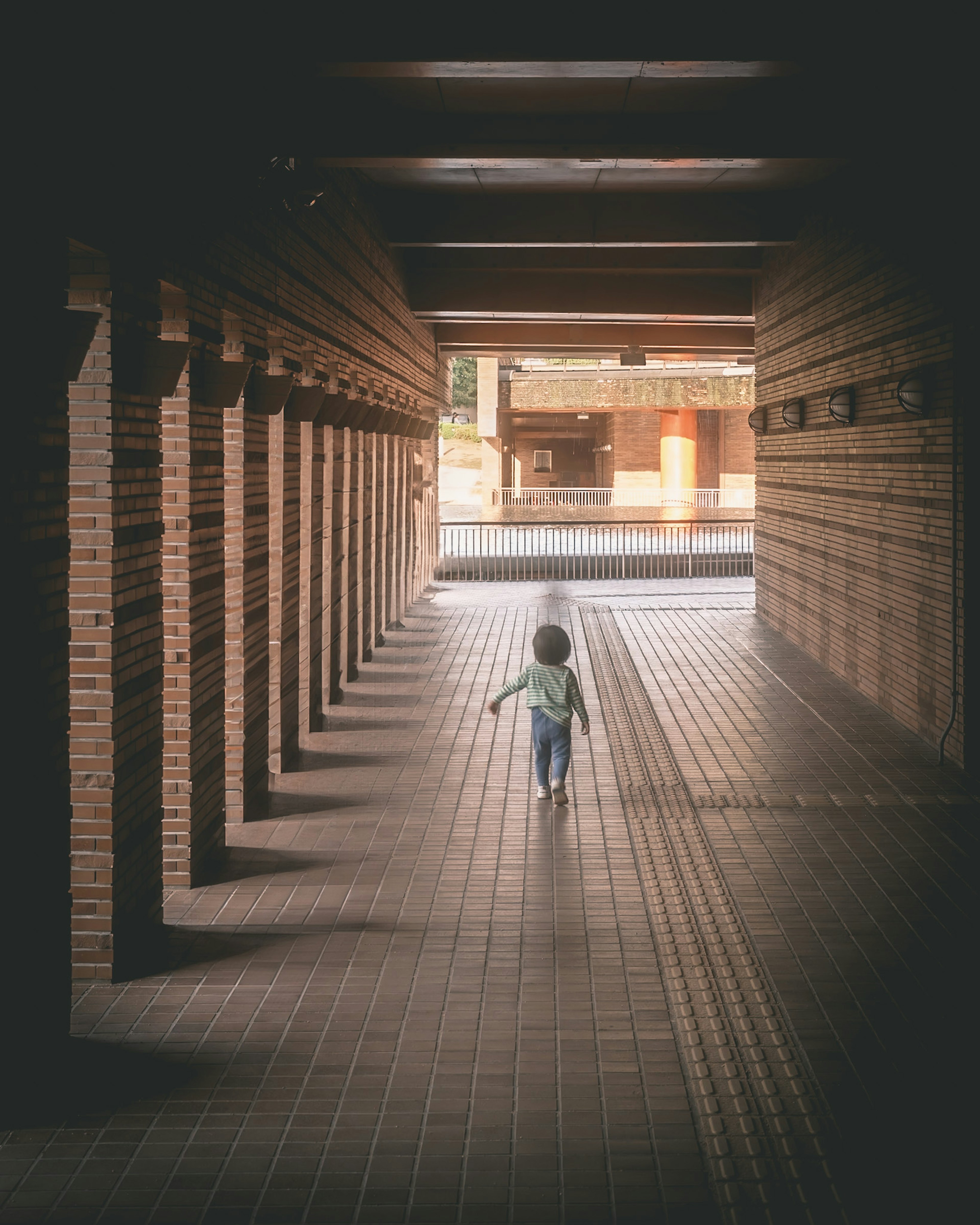 A child walking through a long tunnel with soft lighting and distinctive brick walls