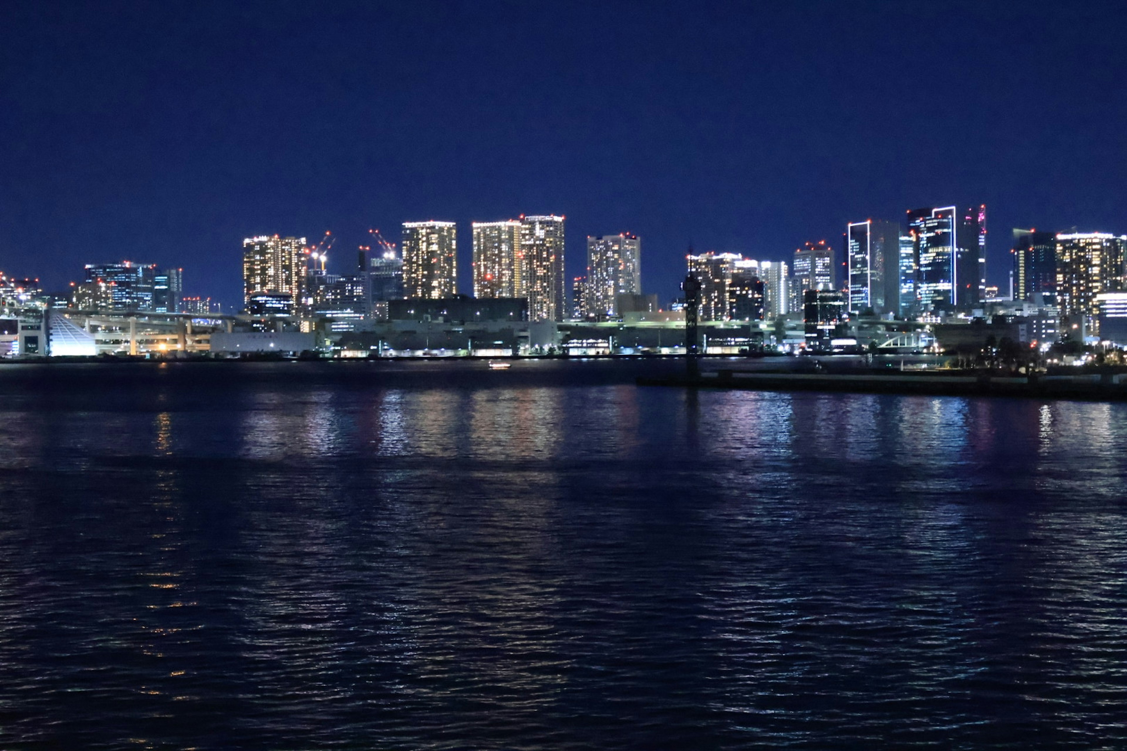 Hermosa vista nocturna de la bahía de Tokio con rascacielos iluminados reflejándose en el agua