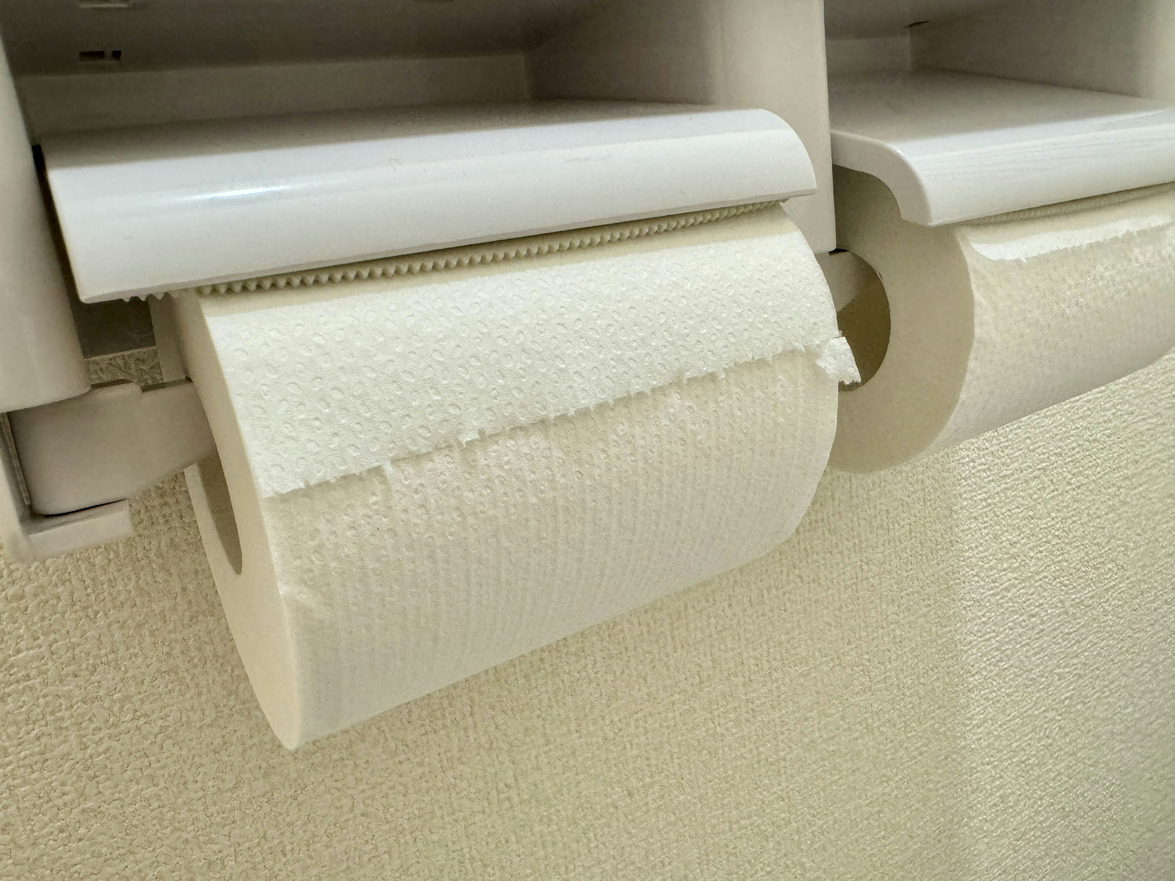 Dos rollos de papel higiénico blanco montados en soportes en una pared texturizada