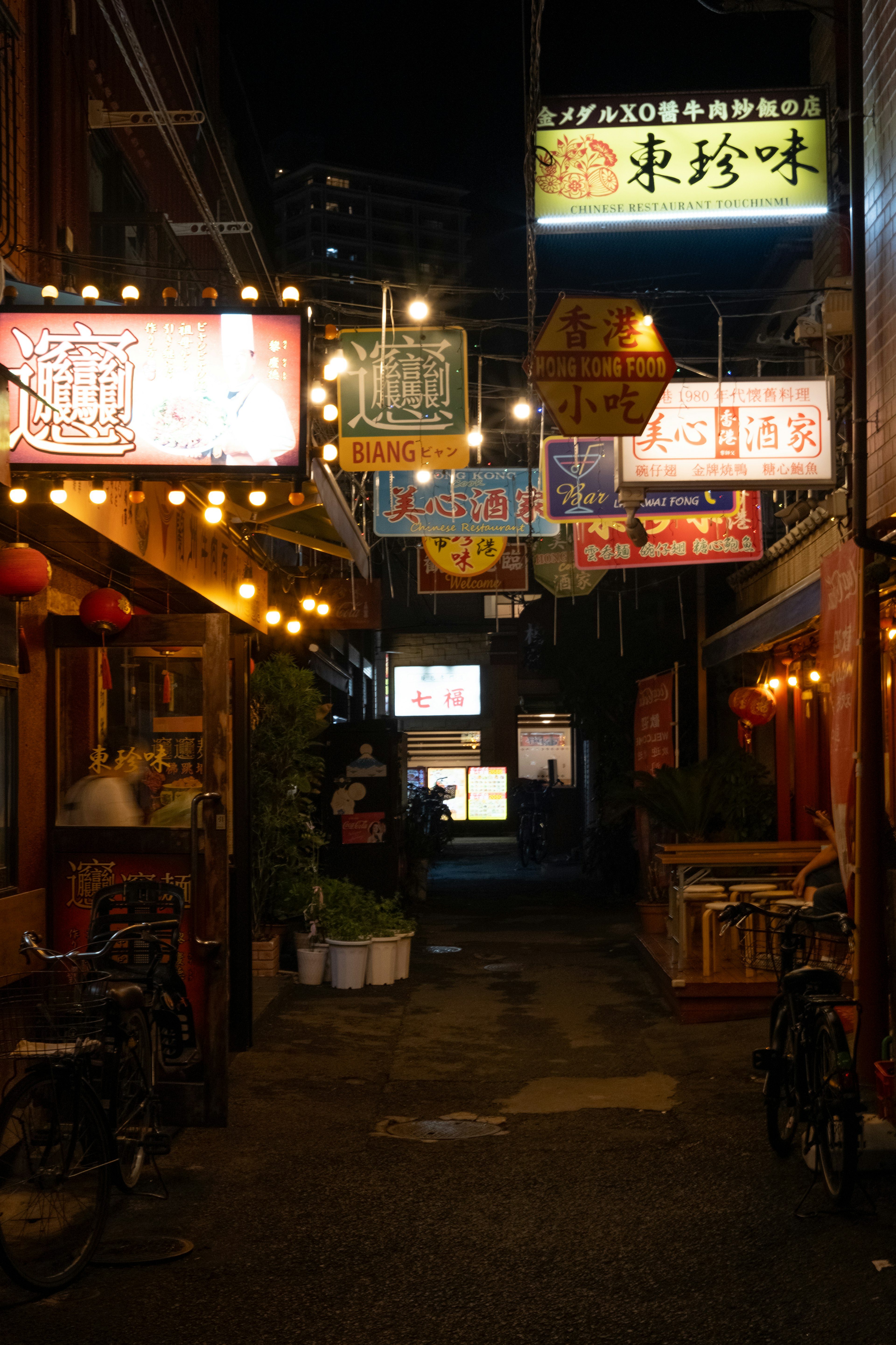 Narrow alley at night lined with restaurant signs and lights