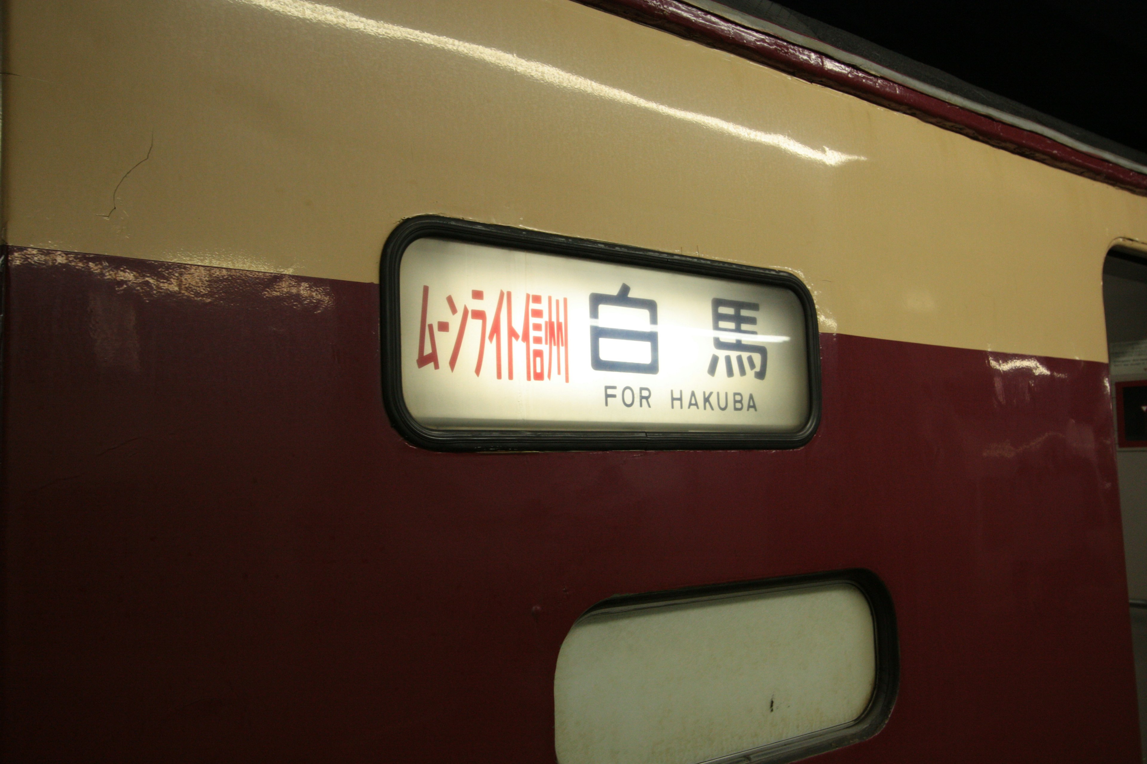 Schild für den Bahnhof Hakuba an einem rot-creamfarbenen Zug