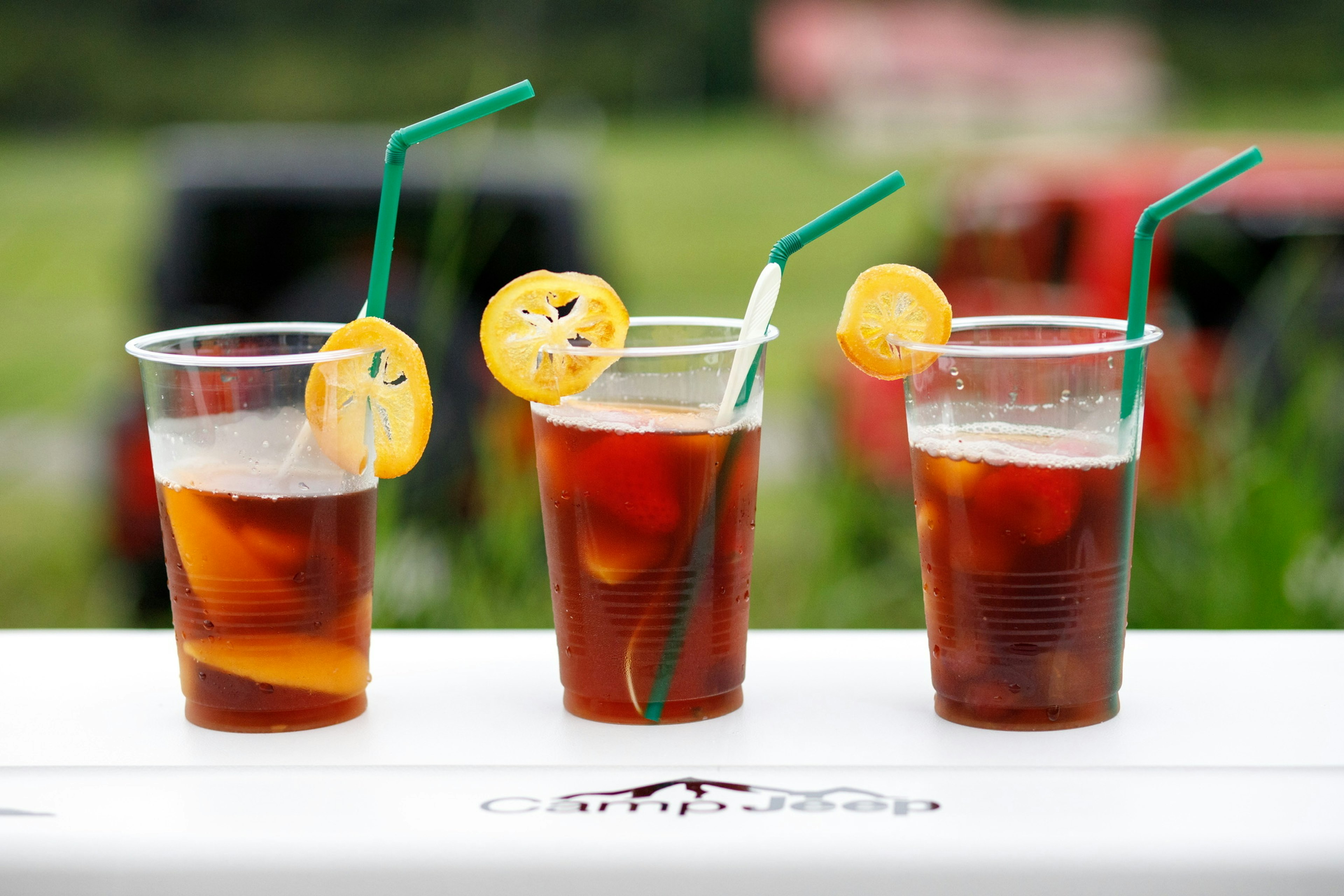 Three transparent cups of iced tea with lemon slices and green straws on a table