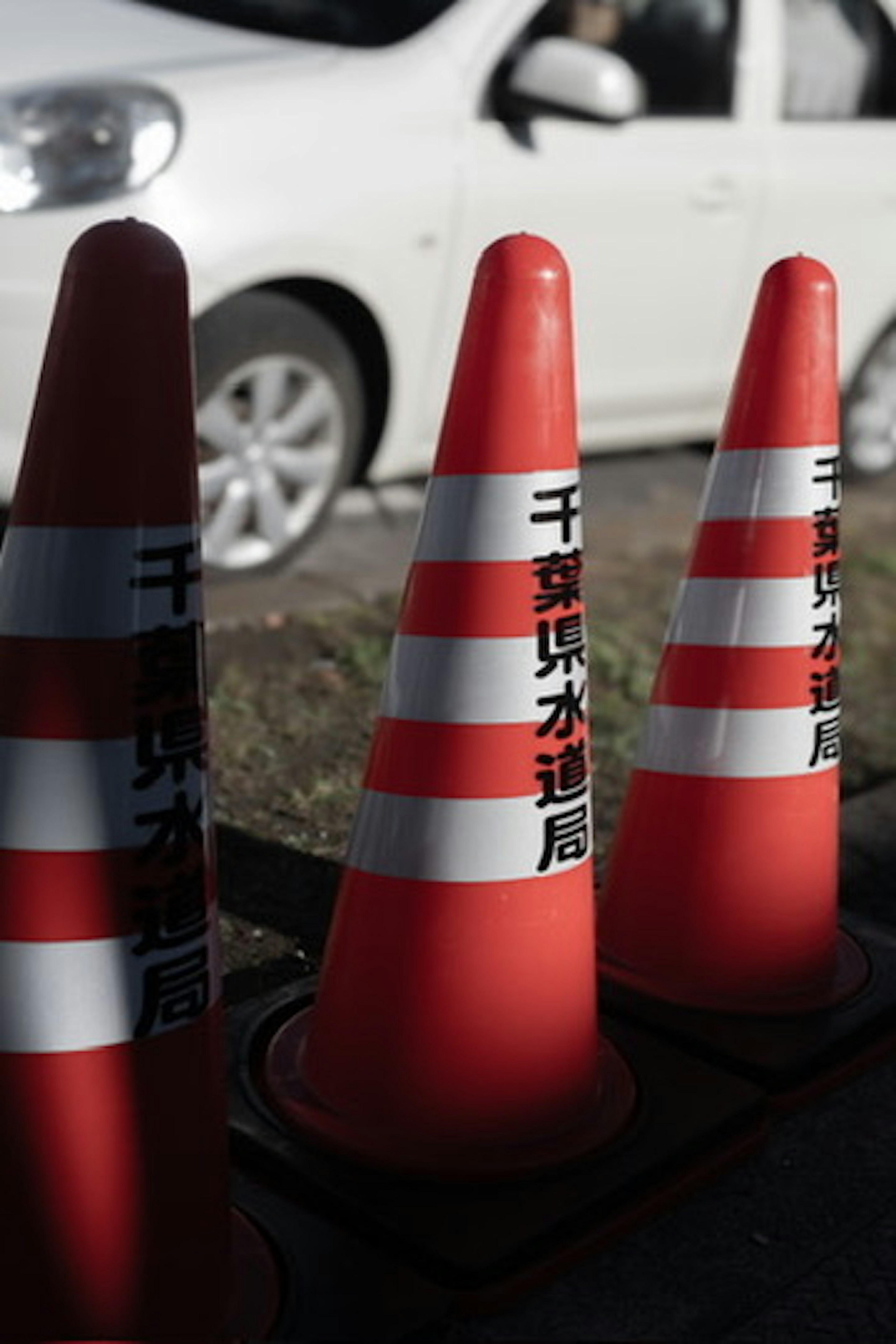 赤い交通コーンが並んでいる横に白い車が停まっている