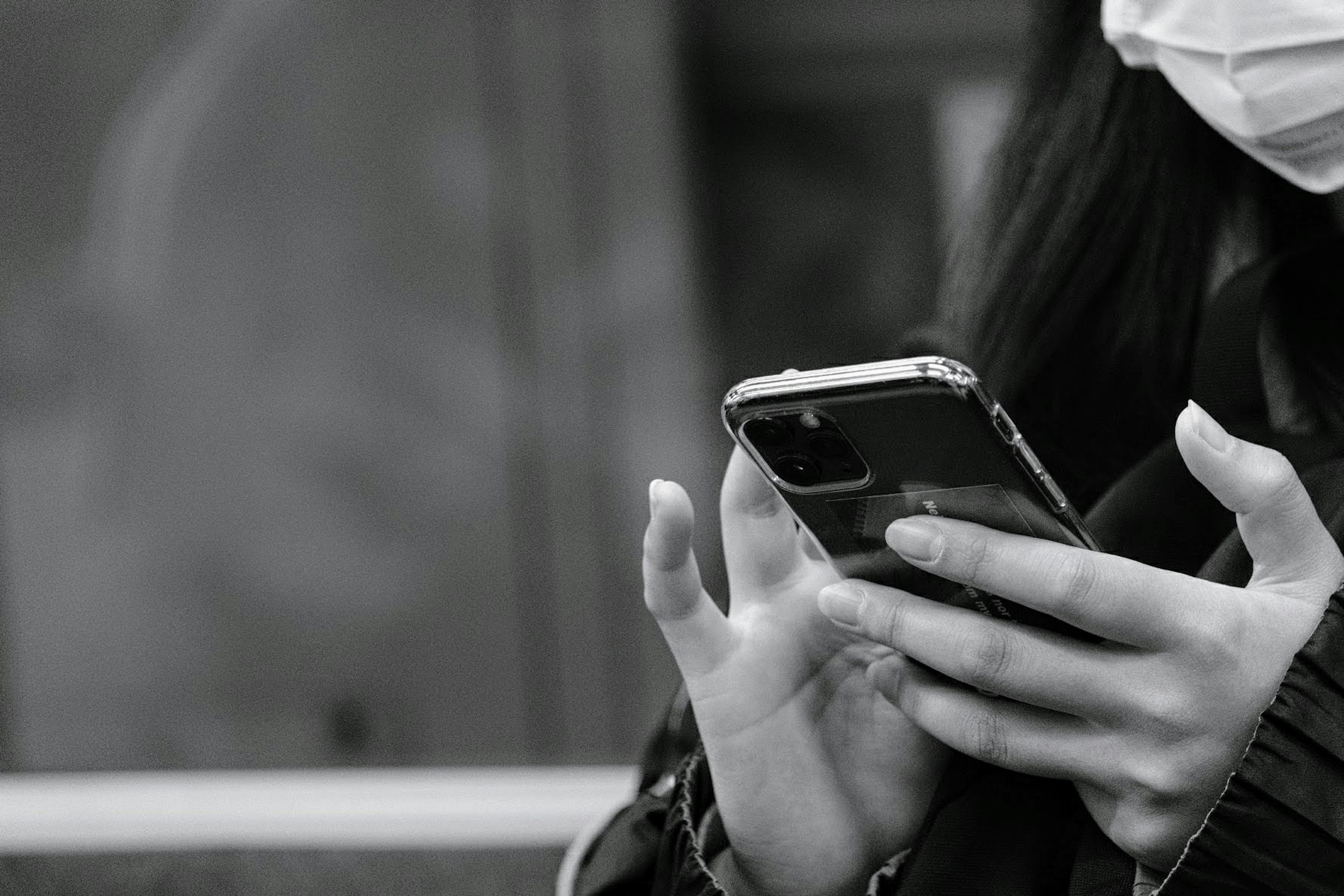 Una persona con mascarilla usando un teléfono inteligente en una imagen en blanco y negro