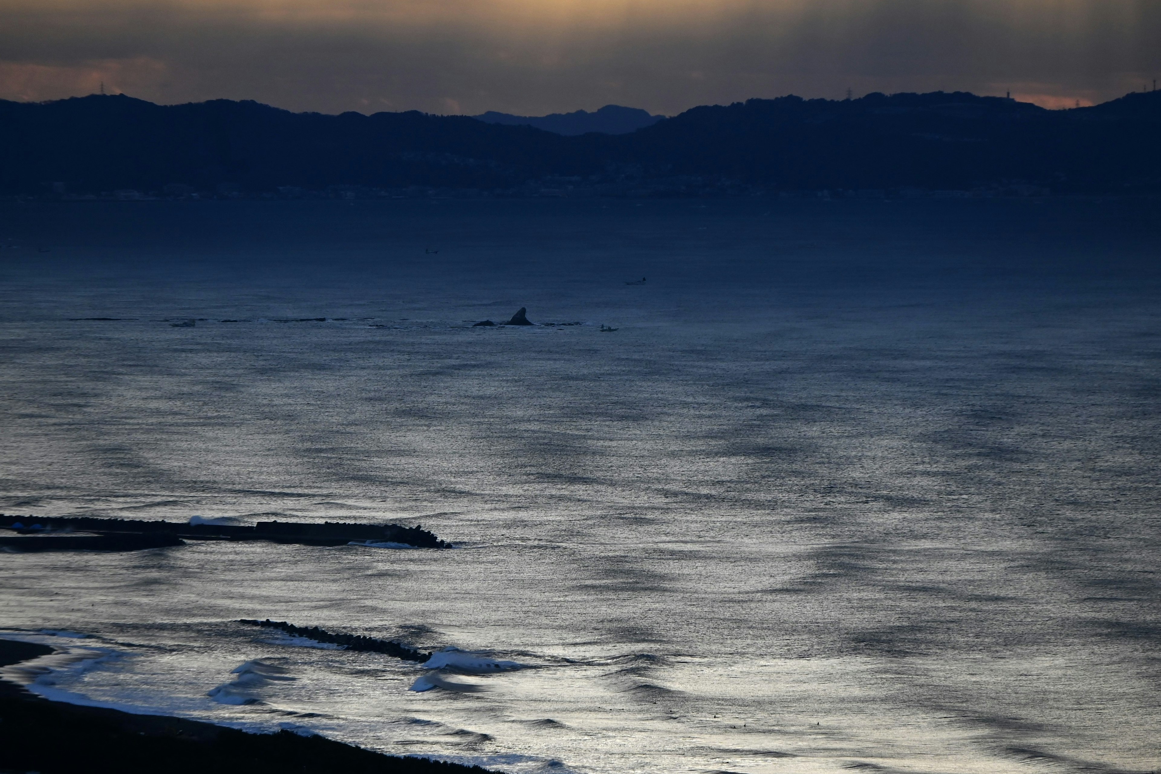 Dämmerungslandschaft mit Meereswellen und Bergsilhouetten