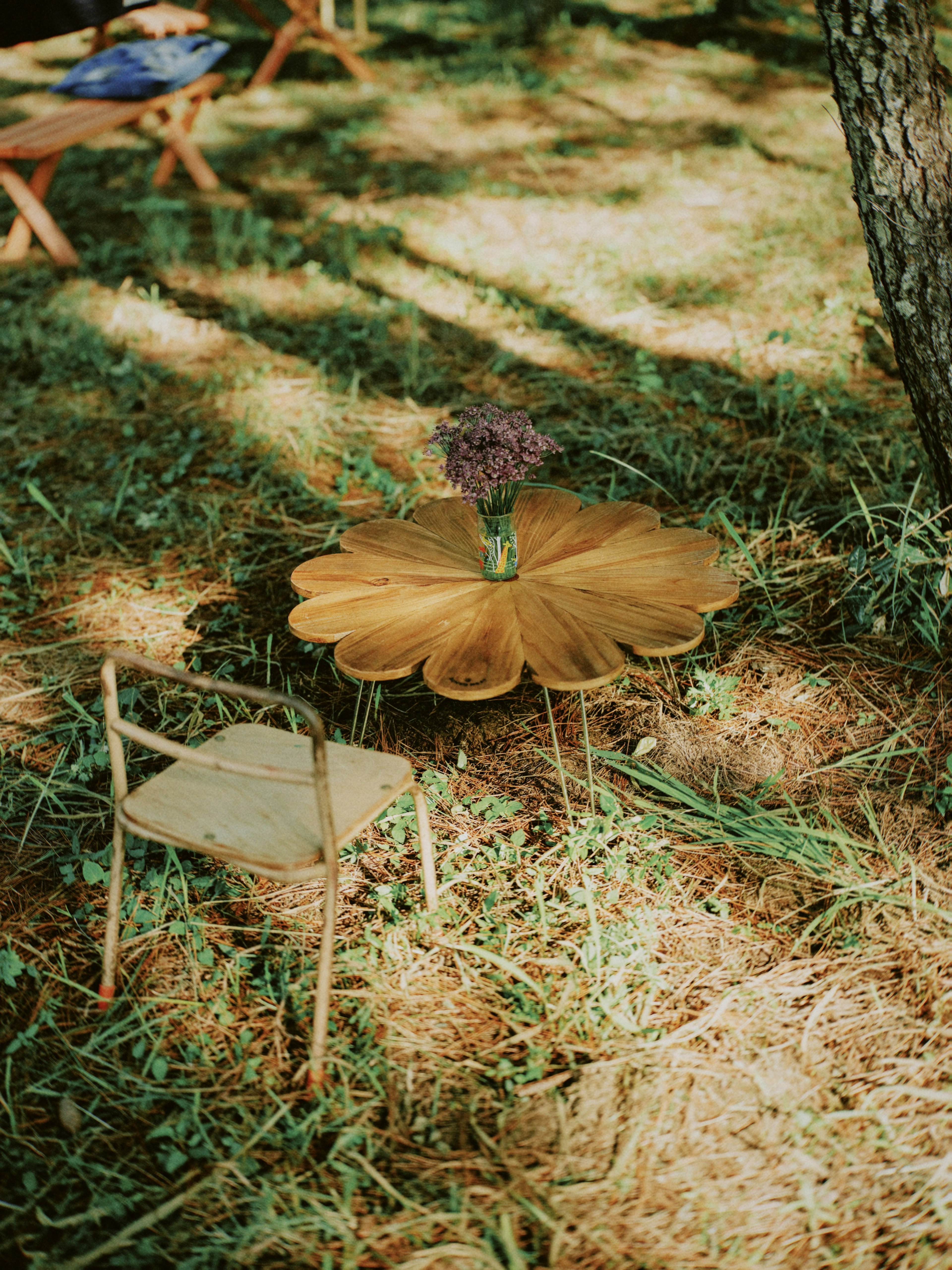 Holztisch in Blumenform mit einer Vase auf dem Gras und einem kleinen Stuhl in der Nähe