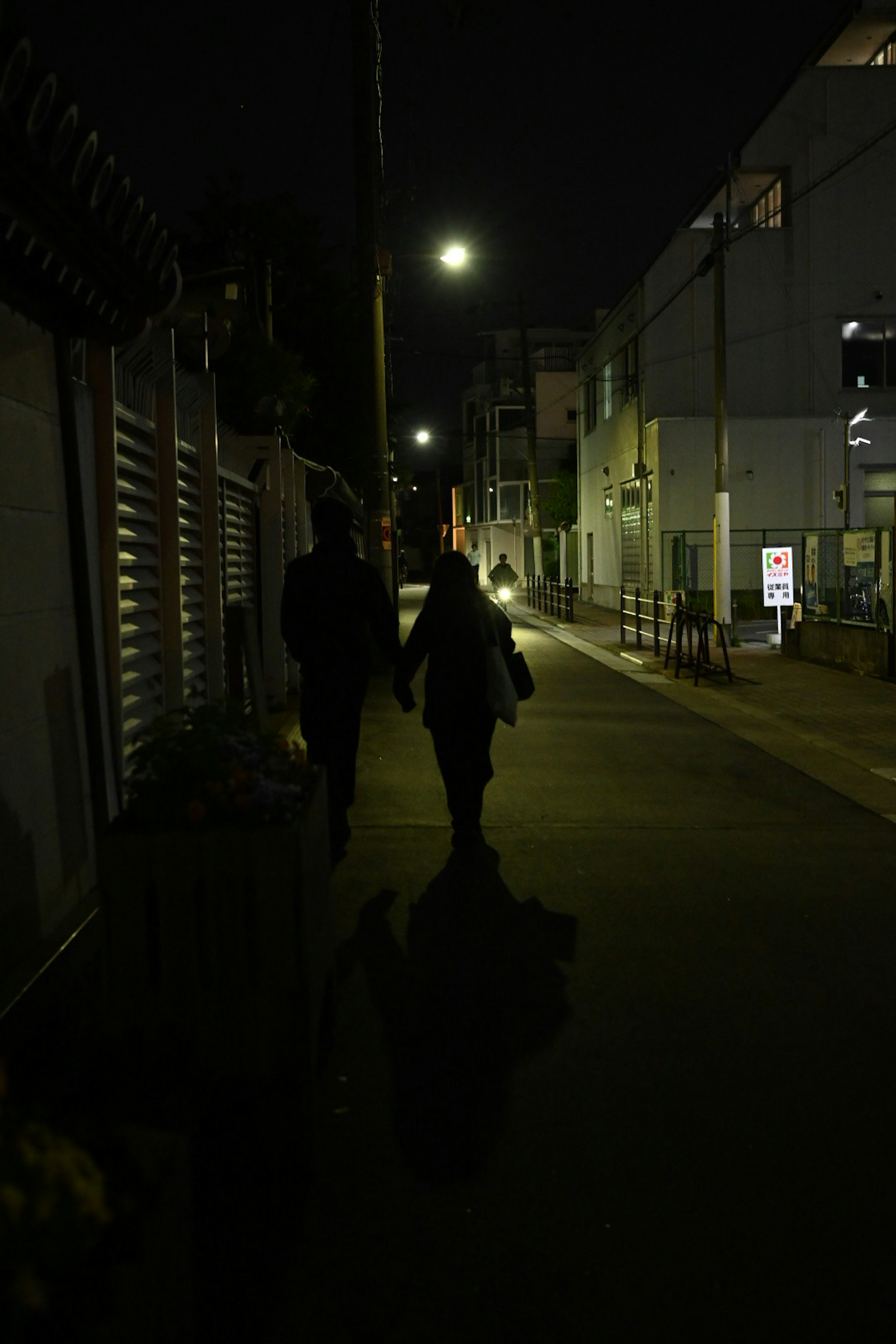 Silhouettes de deux personnes marchant dans une rue sombre éclairée par des lampadaires