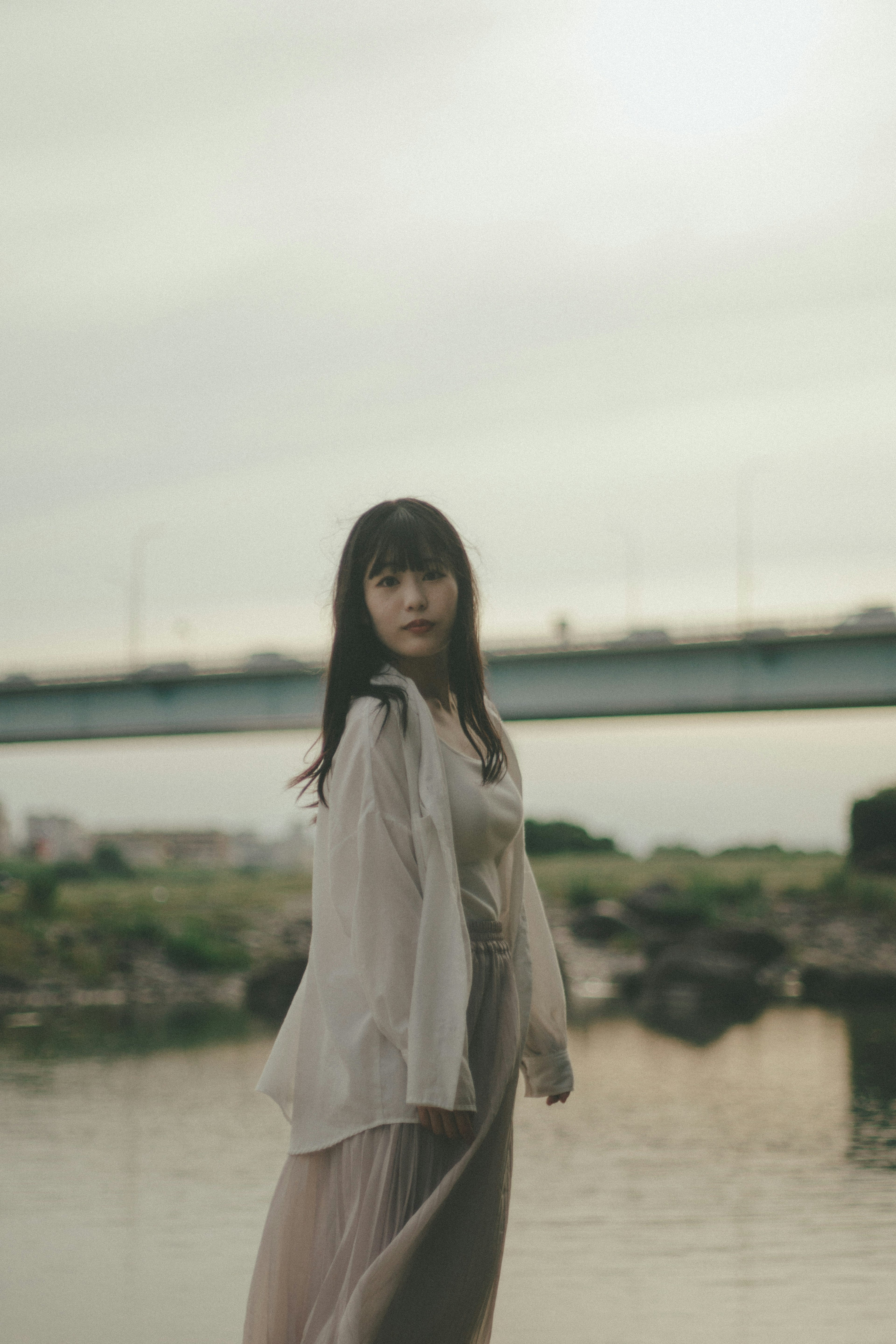 A woman in a light outfit turning around by the riverside