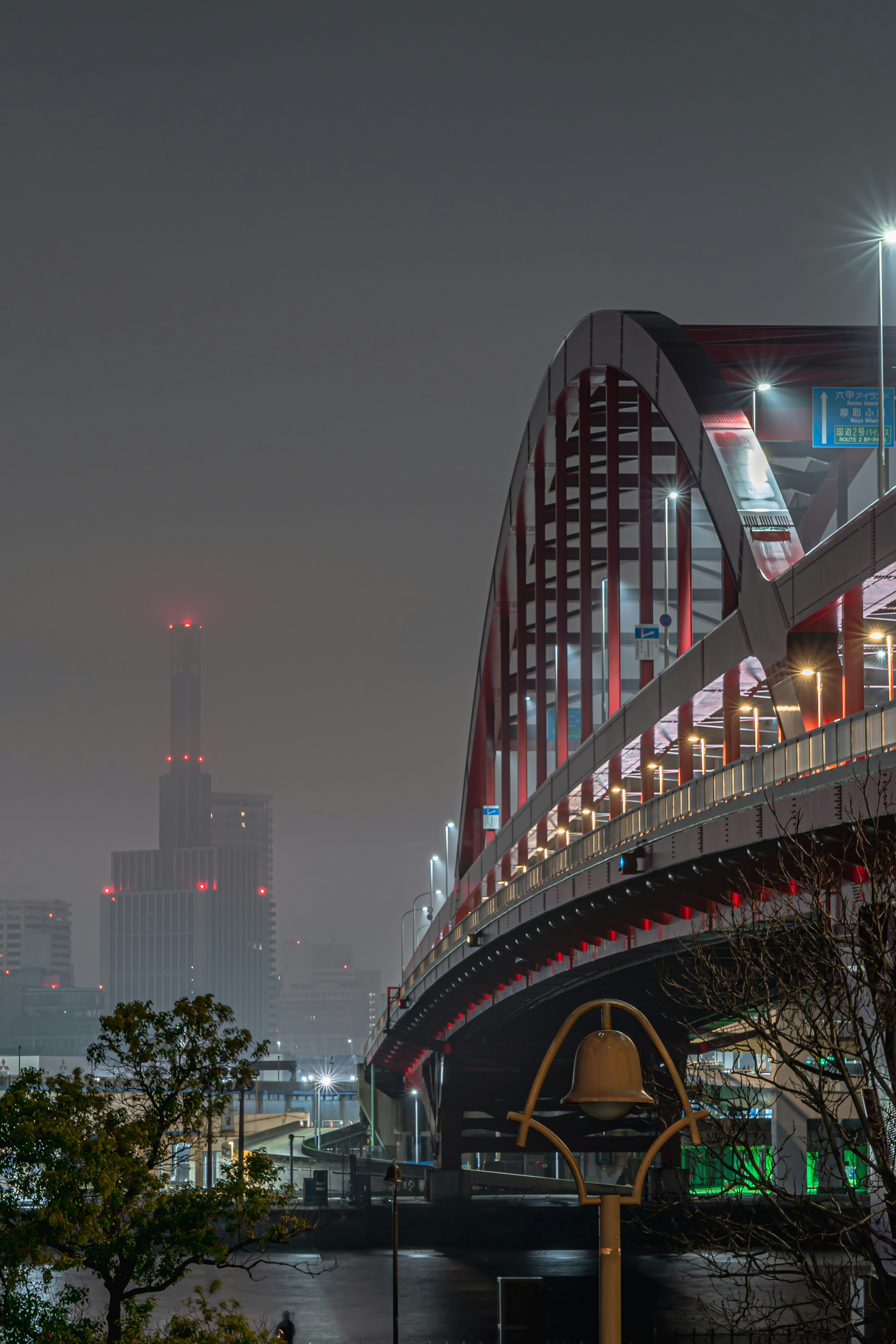 Jembatan lengkung merah dalam pemandangan kota malam dengan gedung pencakar langit di latar belakang