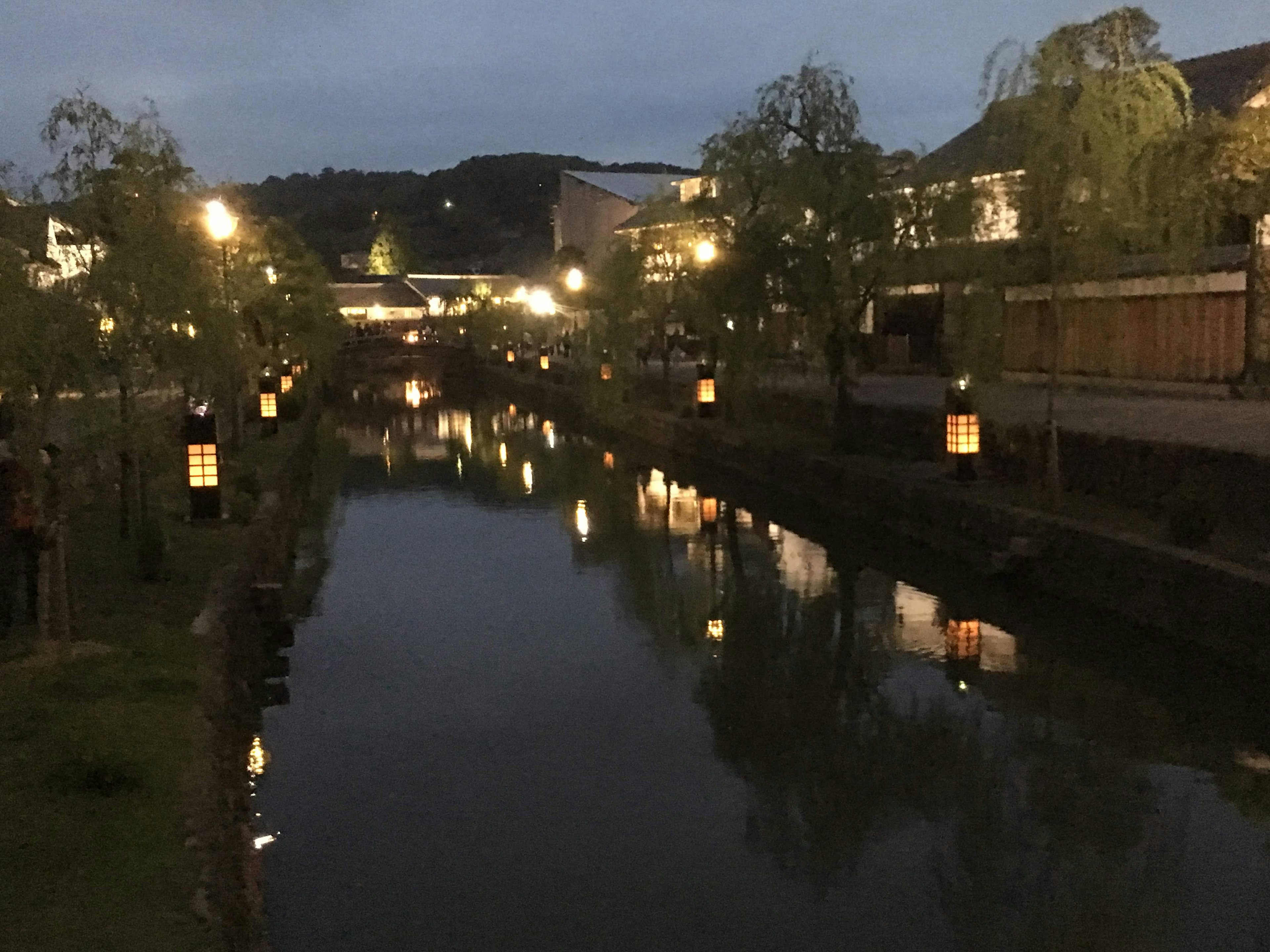 Night scene of a calm river with lanterns and streetlights reflecting on the water