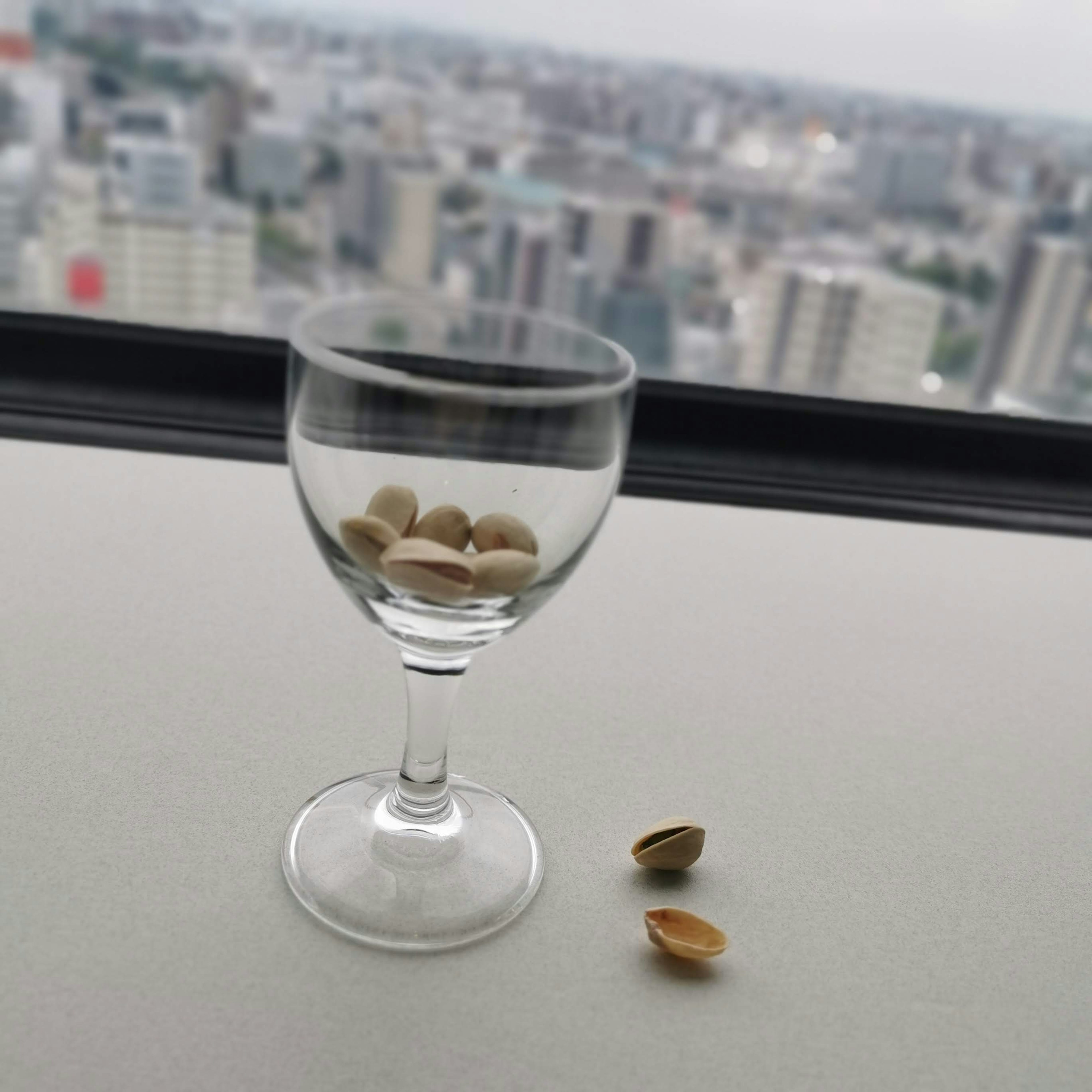 Ein transparentes Glas mit Pistazienhülsen vor einer Stadtlandschaft