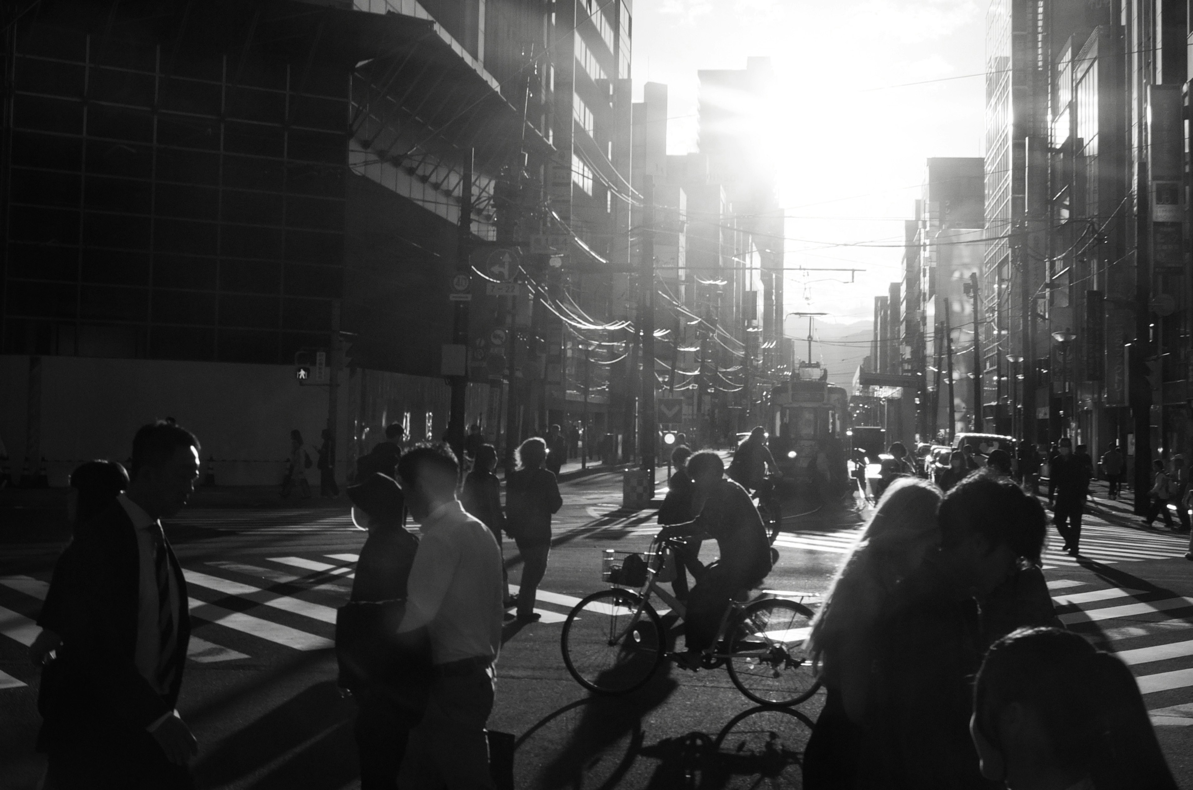 Black and white urban scene with people crossing the street a cyclist in the foreground and tall buildings in the background