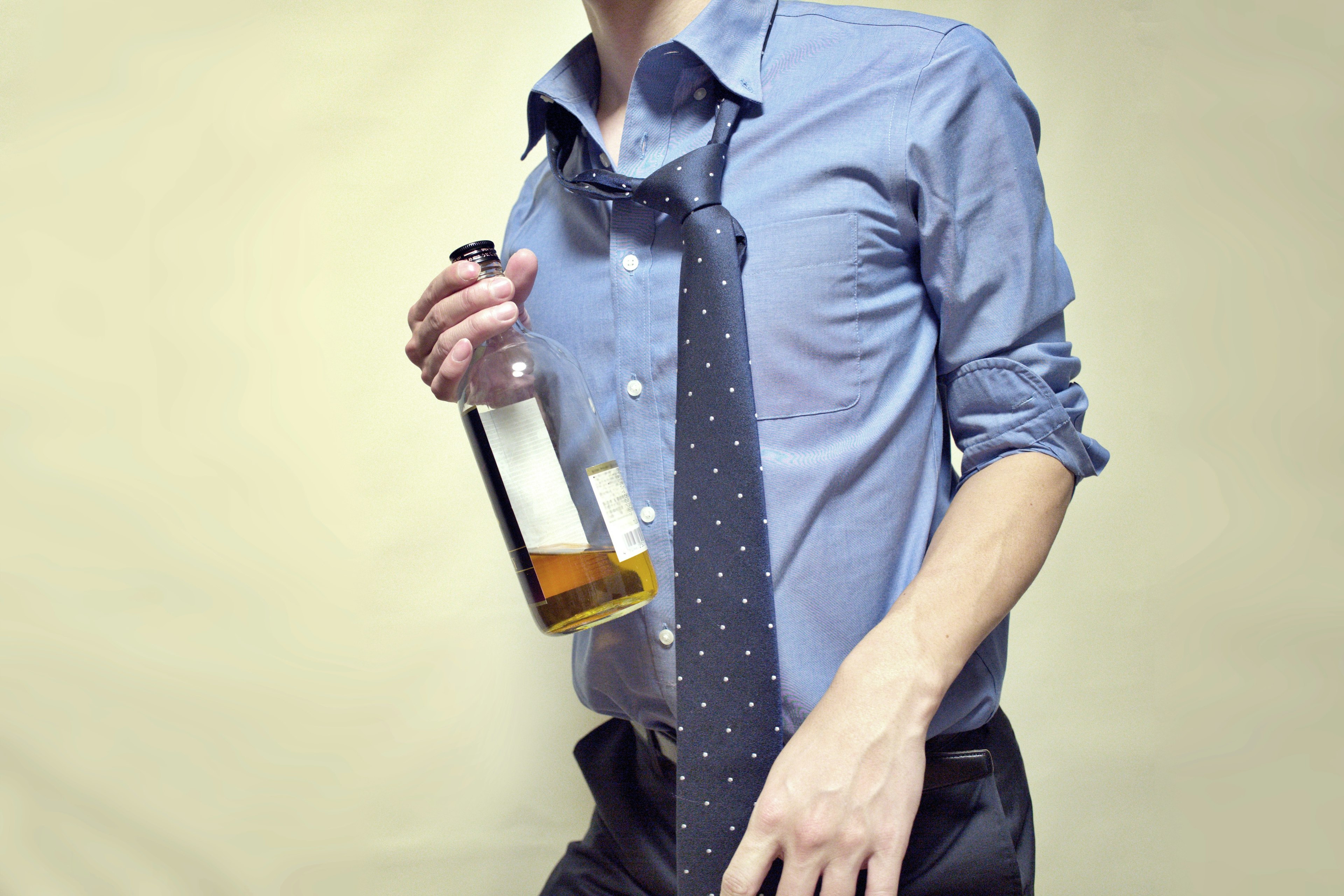 A man in a blue shirt and tie holding a bottle of liquor