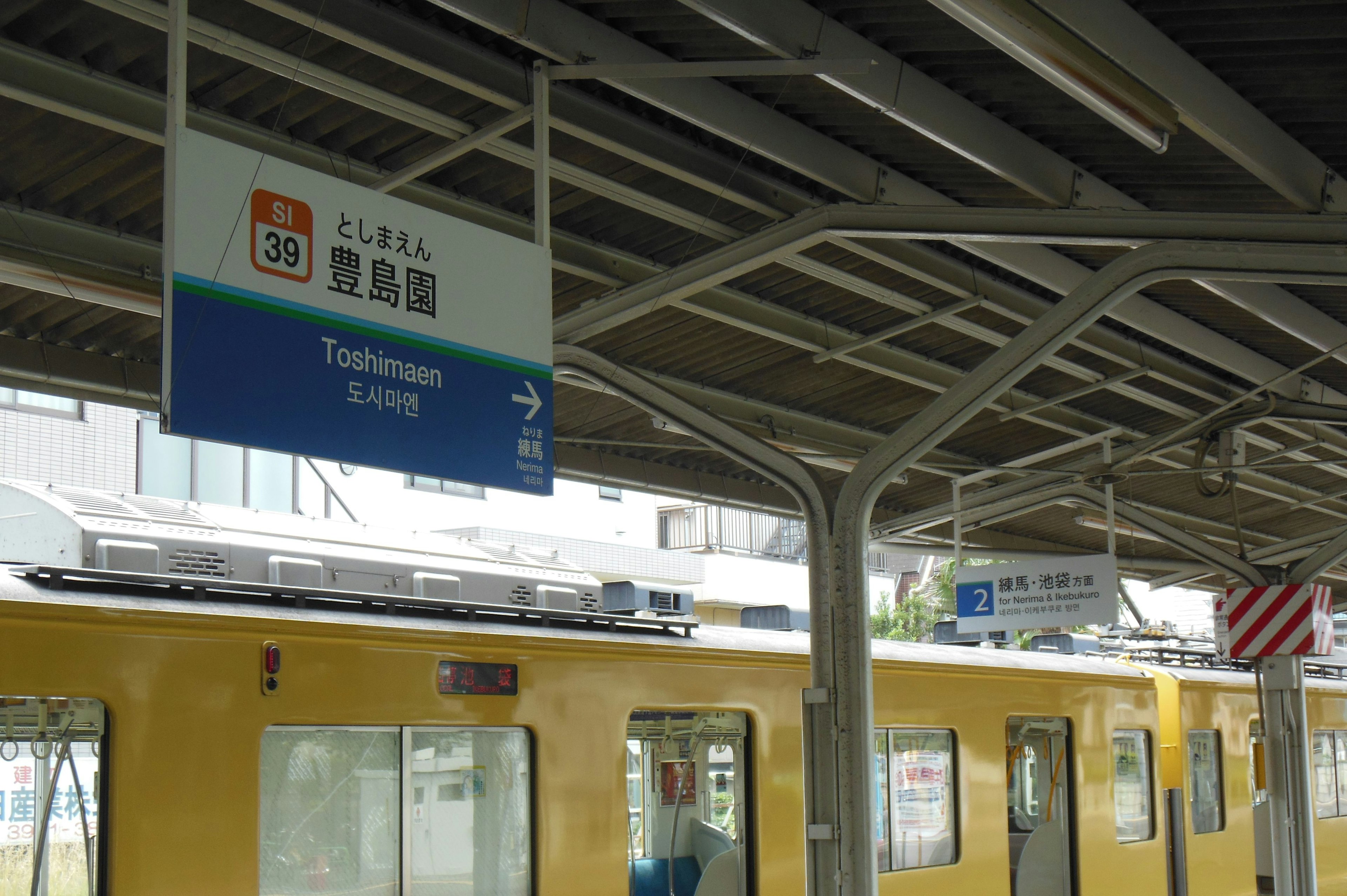 Señal de plataforma en una estación de tren con un tren amarillo