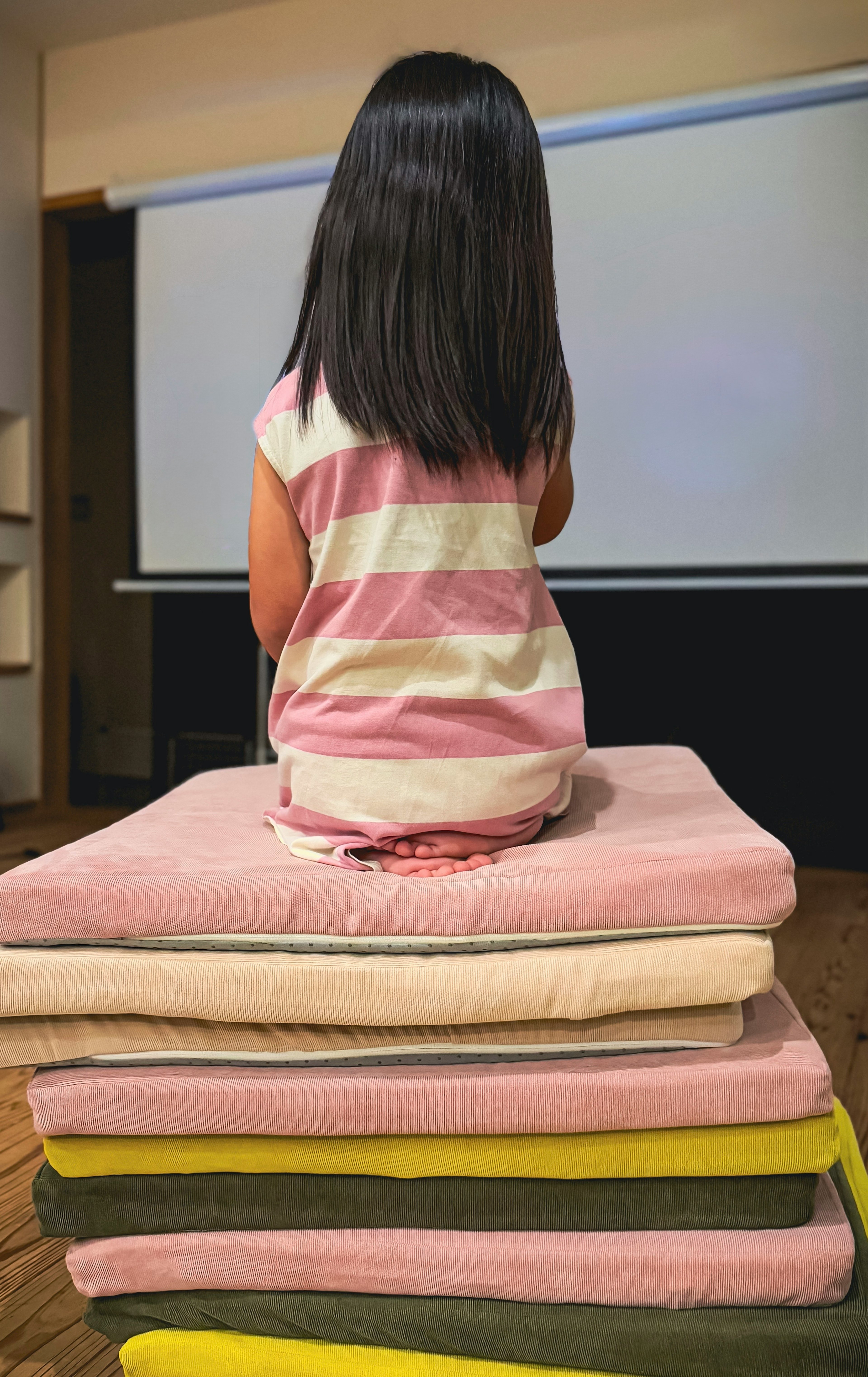 A girl in a striped shirt sitting on stacked blankets