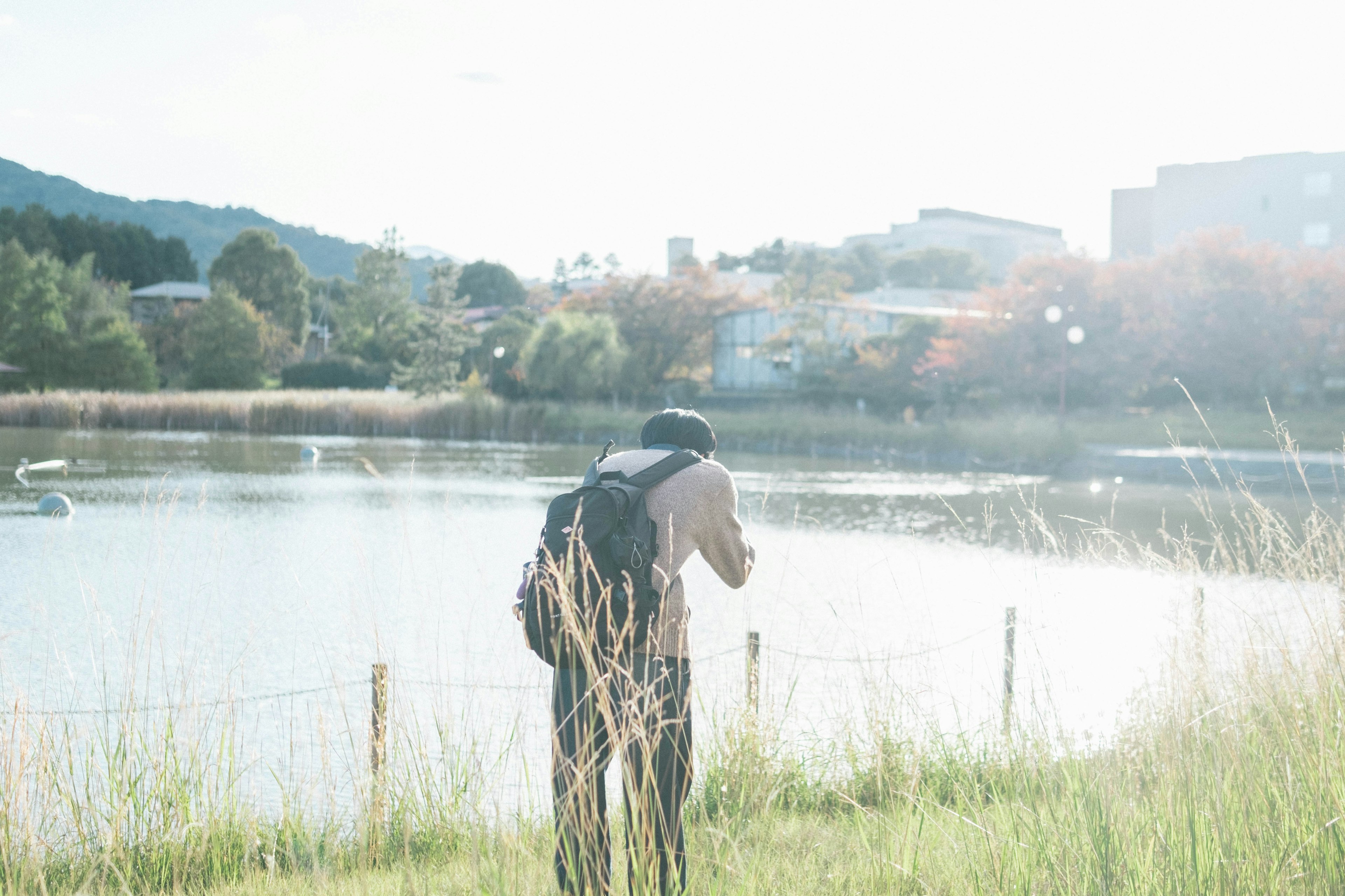 Silhouette of a man with a camera near a lake with mountains and buildings in the background