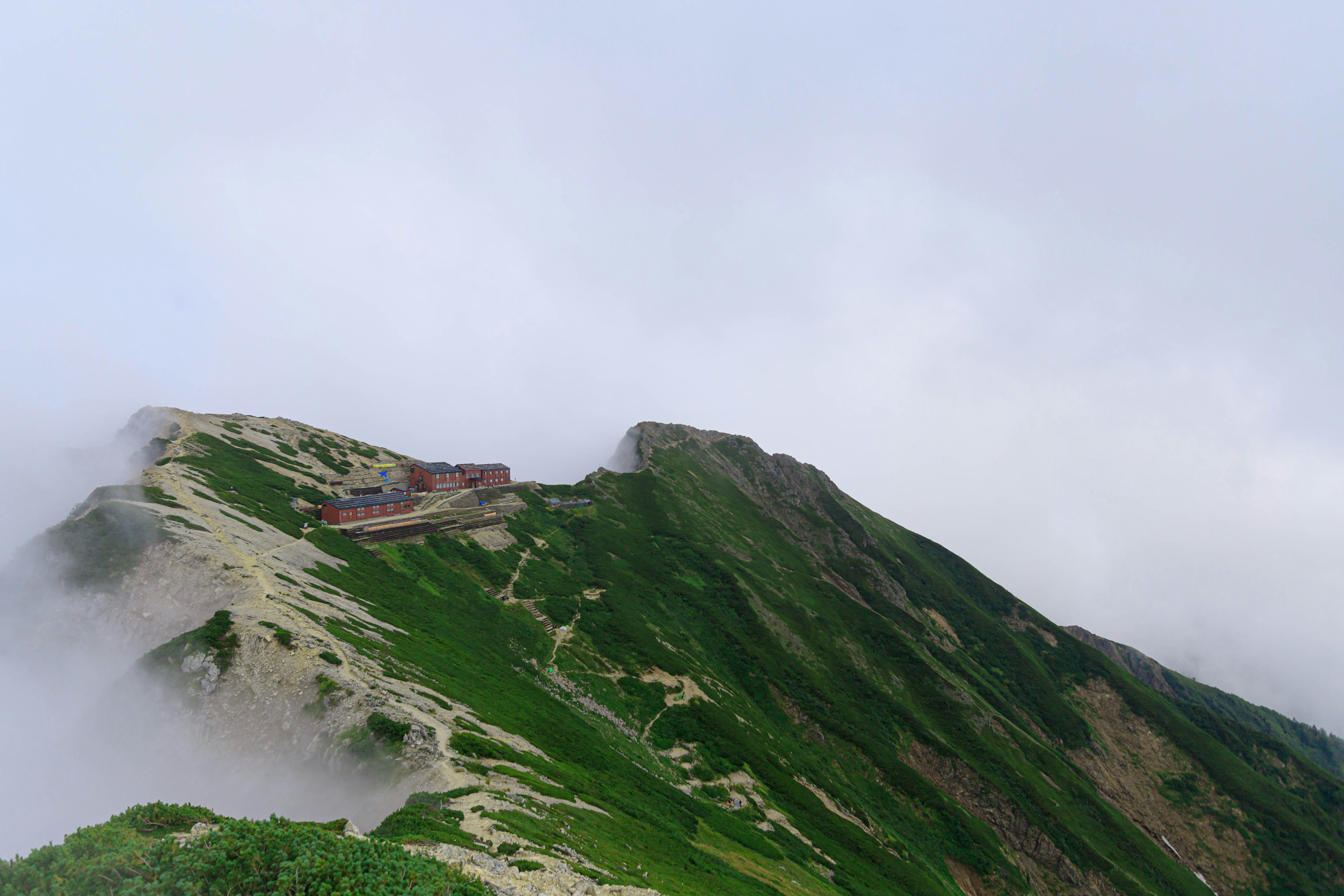 霧に包まれた山の斜面にある建物と緑の草原