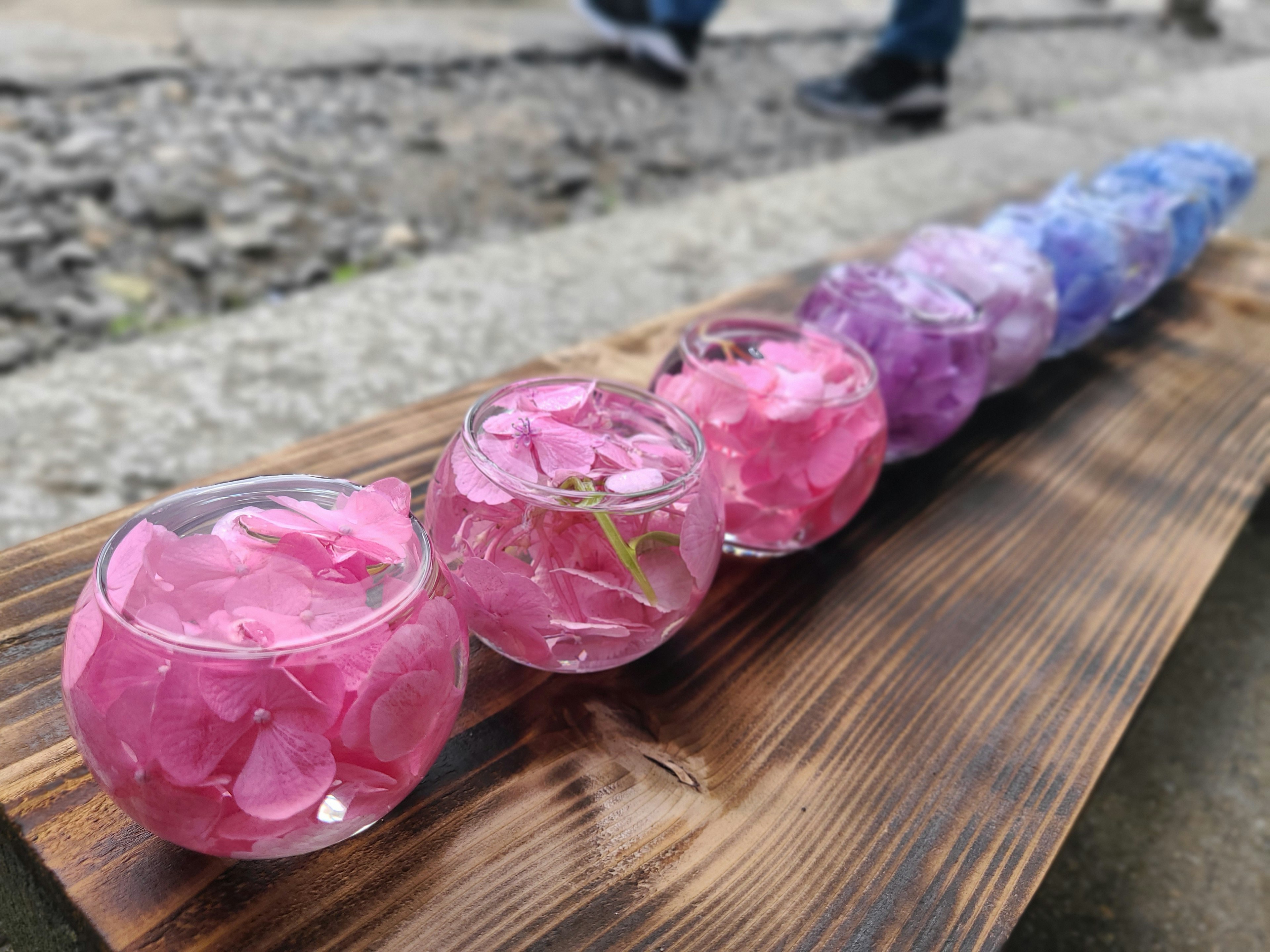 Tazones de vidrio con pétalos de flores rosas y moradas dispuestos en una bandeja de madera