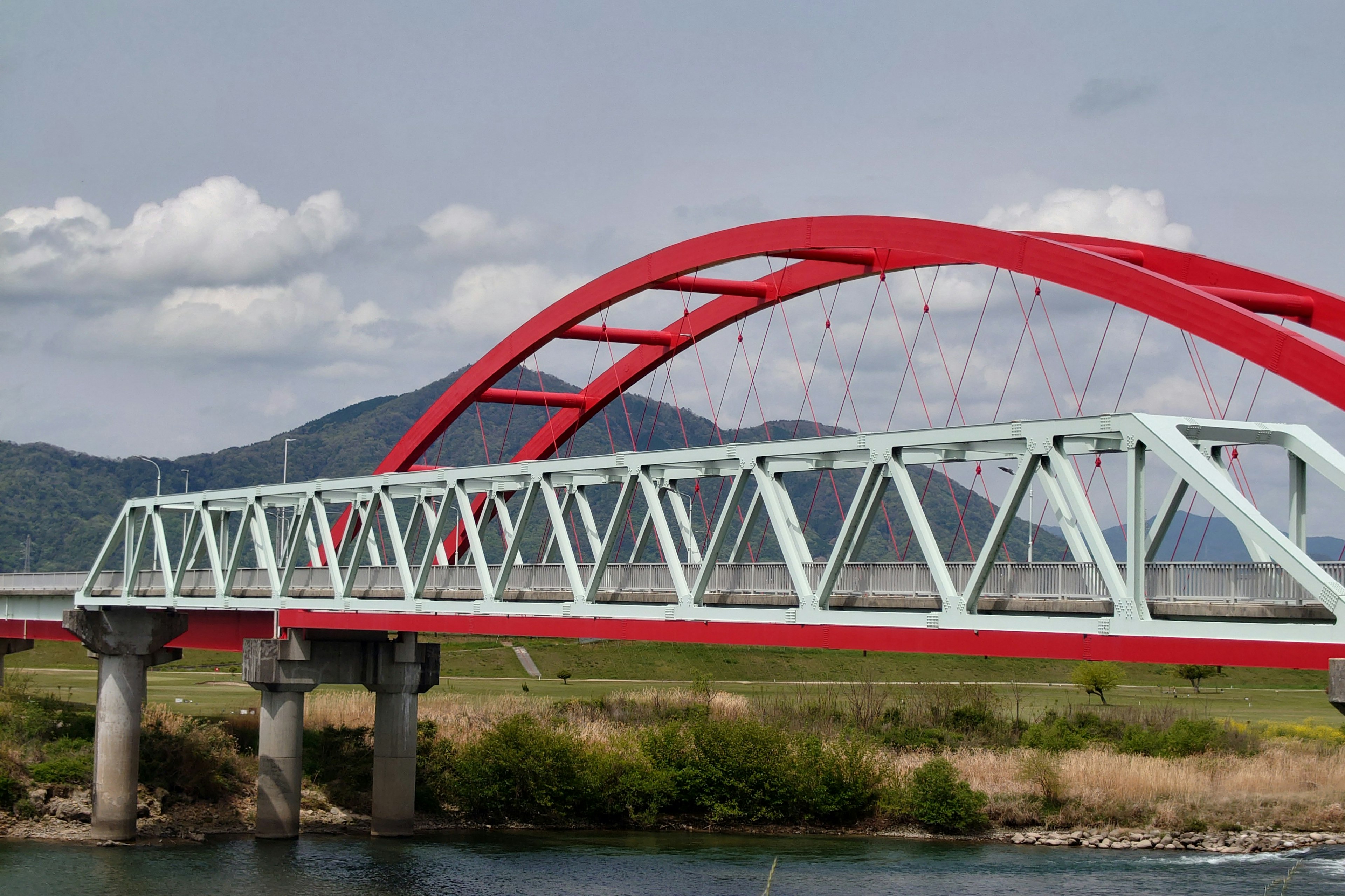 Rote Bogenbrücke und blaue Fachwerkbrücke über einen Fluss