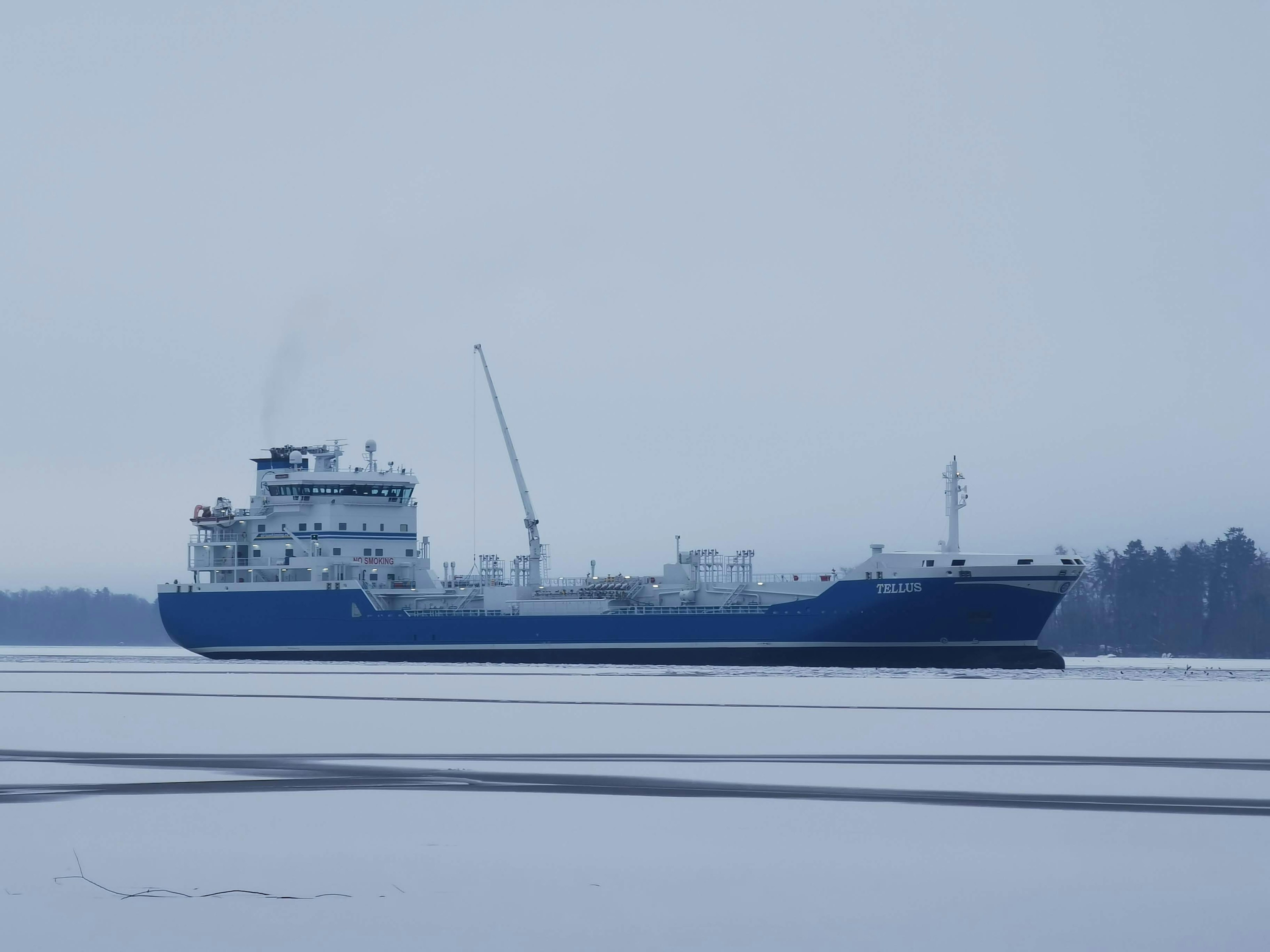 Blue cargo ship navigating through ice with snowy landscape