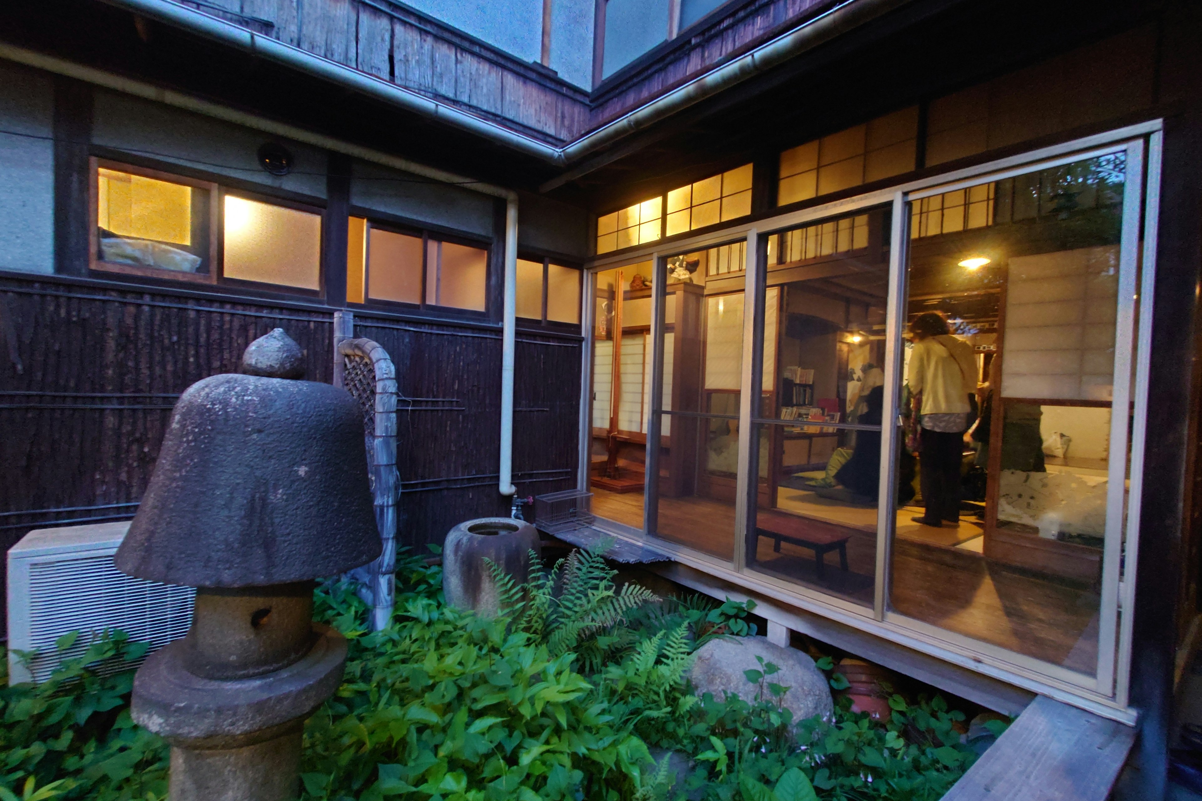 Jardin d'une maison japonaise traditionnelle au crépuscule avec une lanterne en pierre et une végétation luxuriante