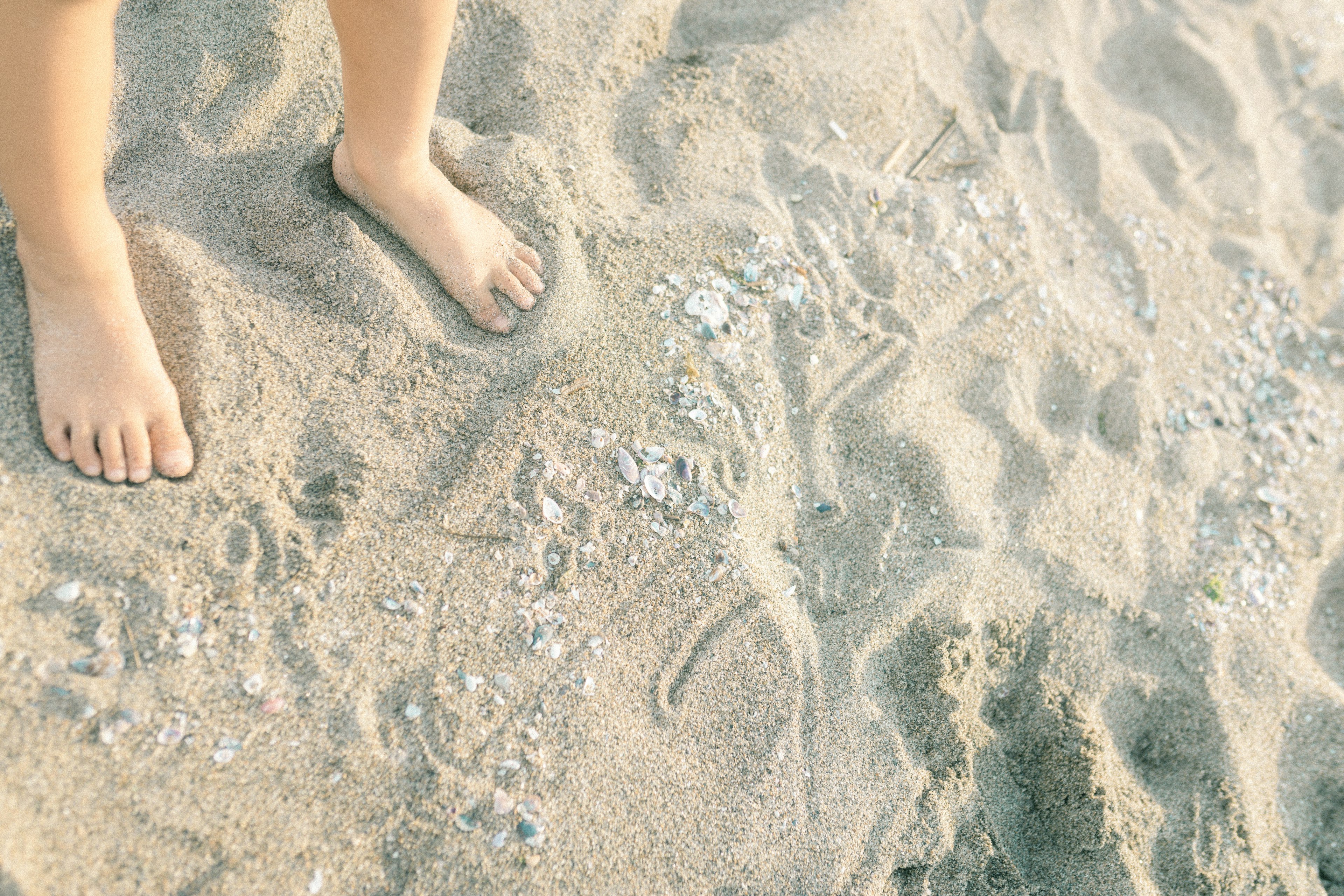 Barfuß stehende Füße eines Kindes im Sand mit Mustern im Sand