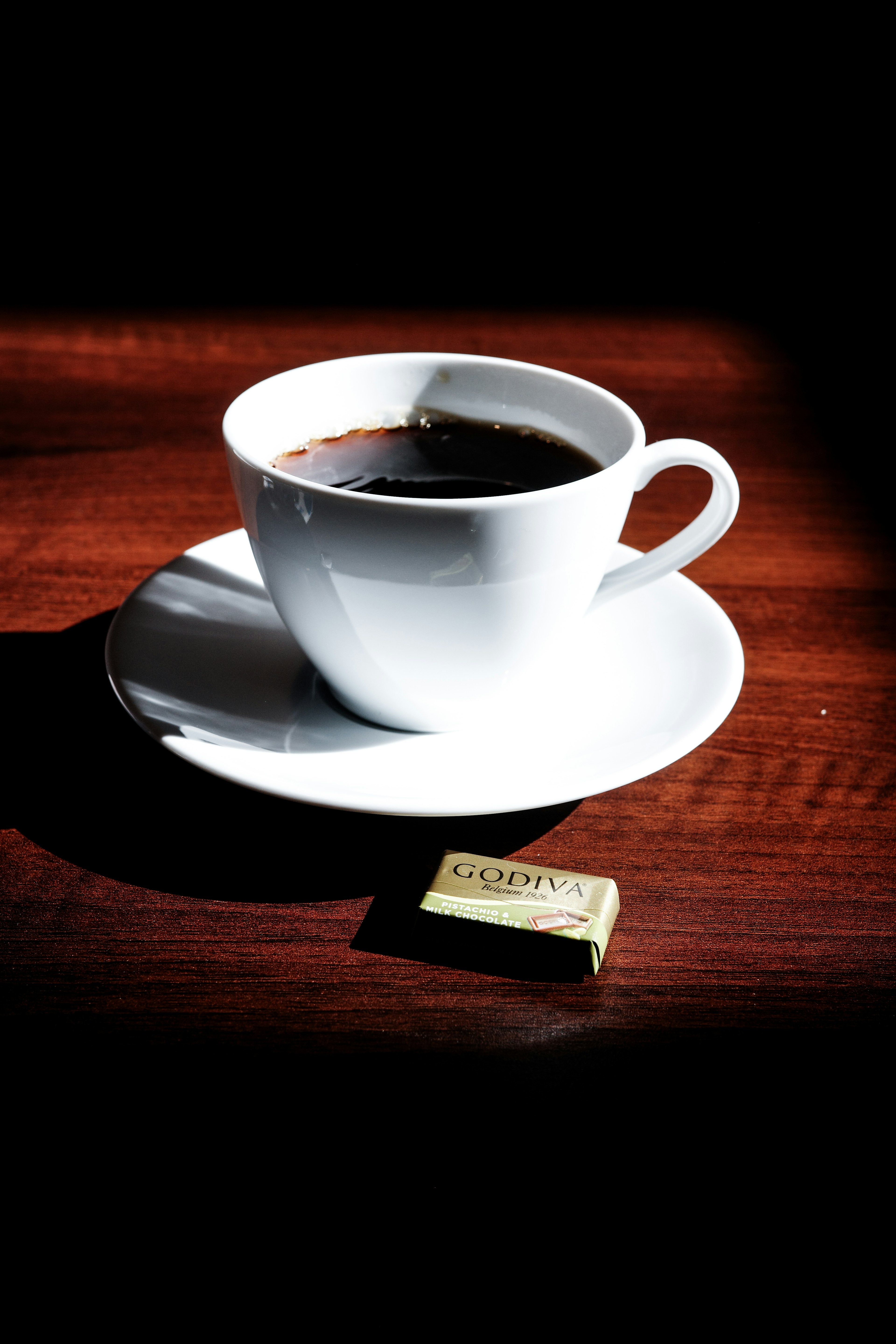 White coffee cup with saucer filled with coffee and a piece of chocolate