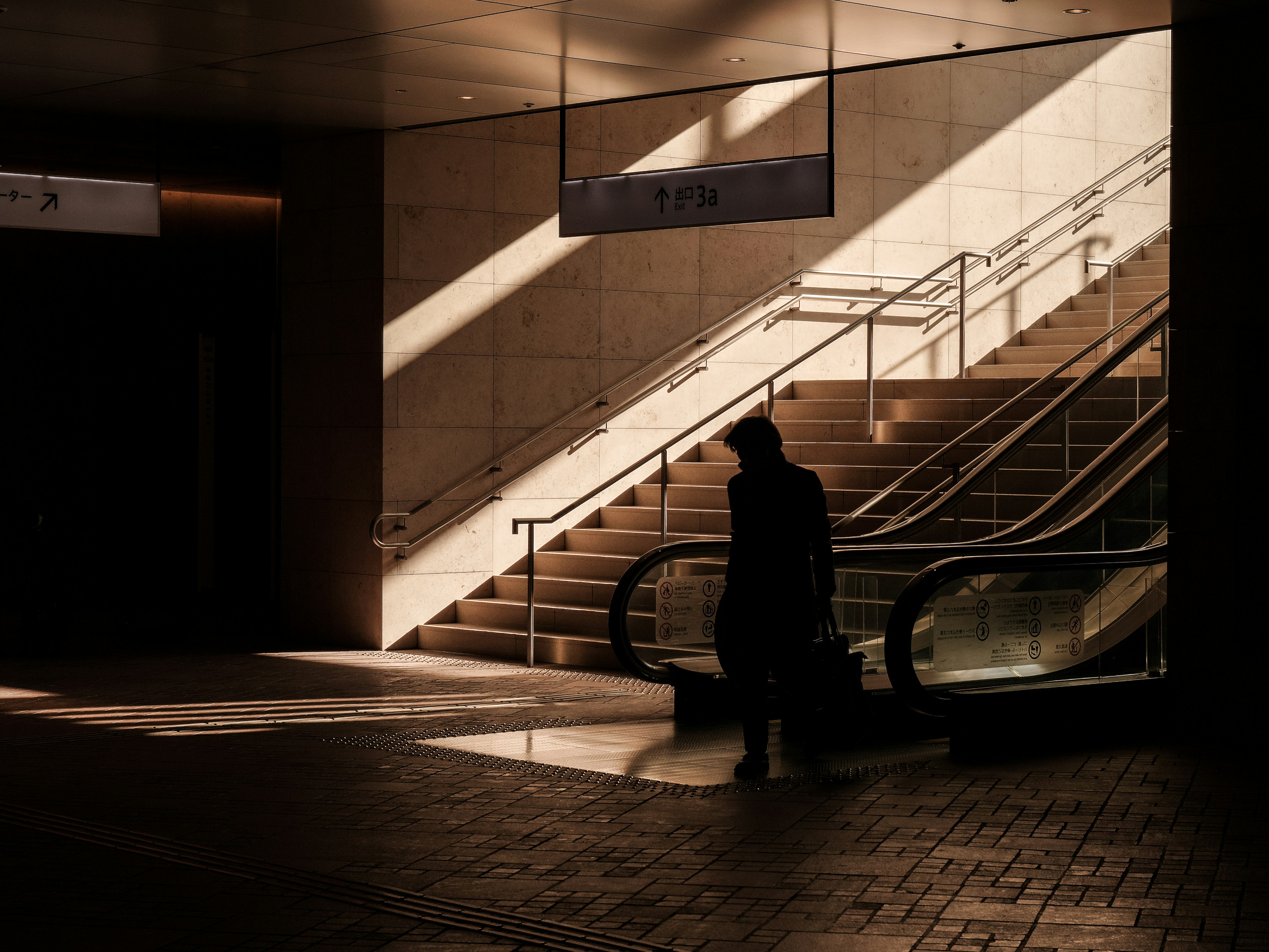 Une personne se tenant dans l'ombre dans un intérieur moderne bien éclairé avec des escaliers et un escalator