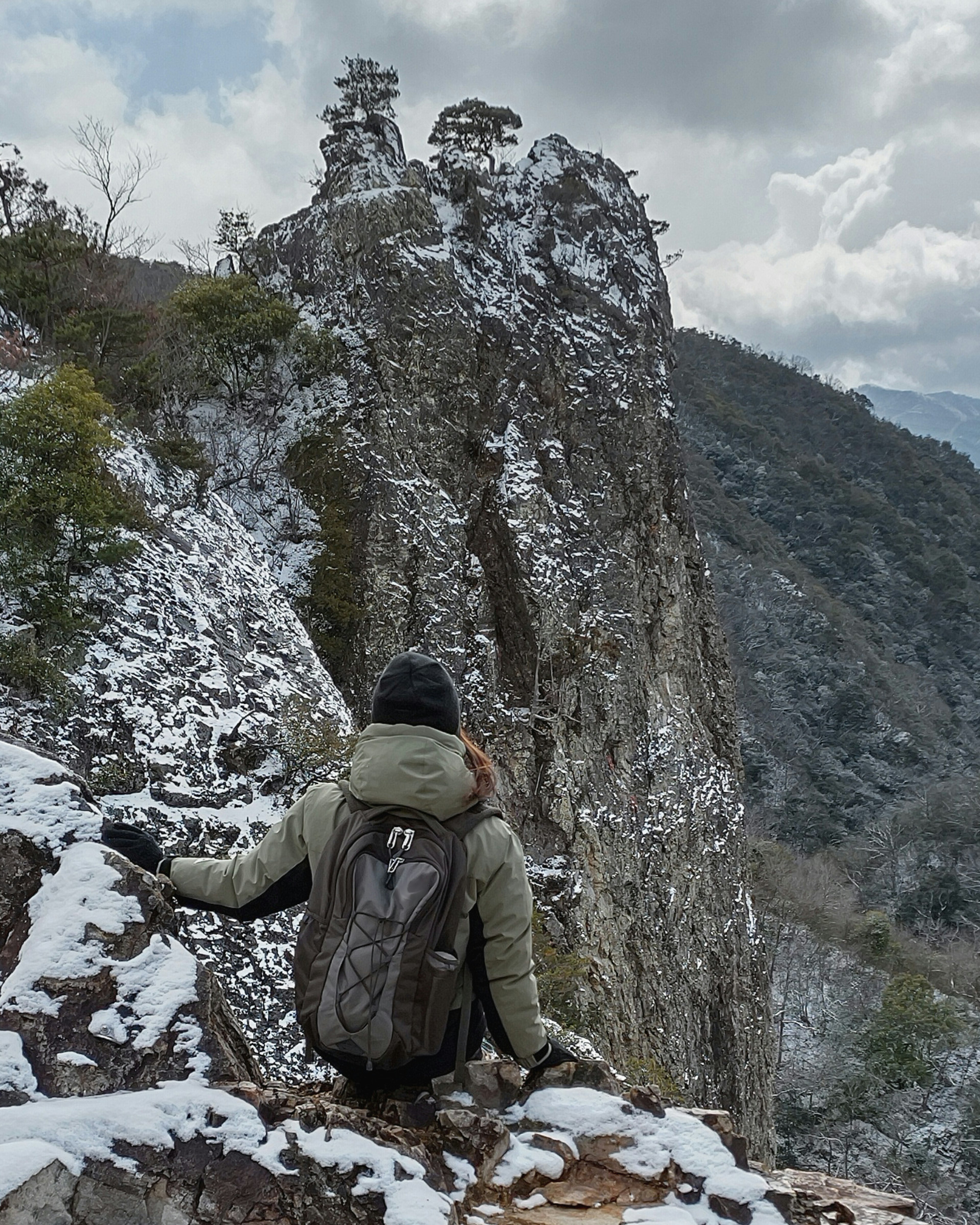 Wanderer sitzt auf einem schneebedeckten Bergrücken und schaut auf felsige Gipfel