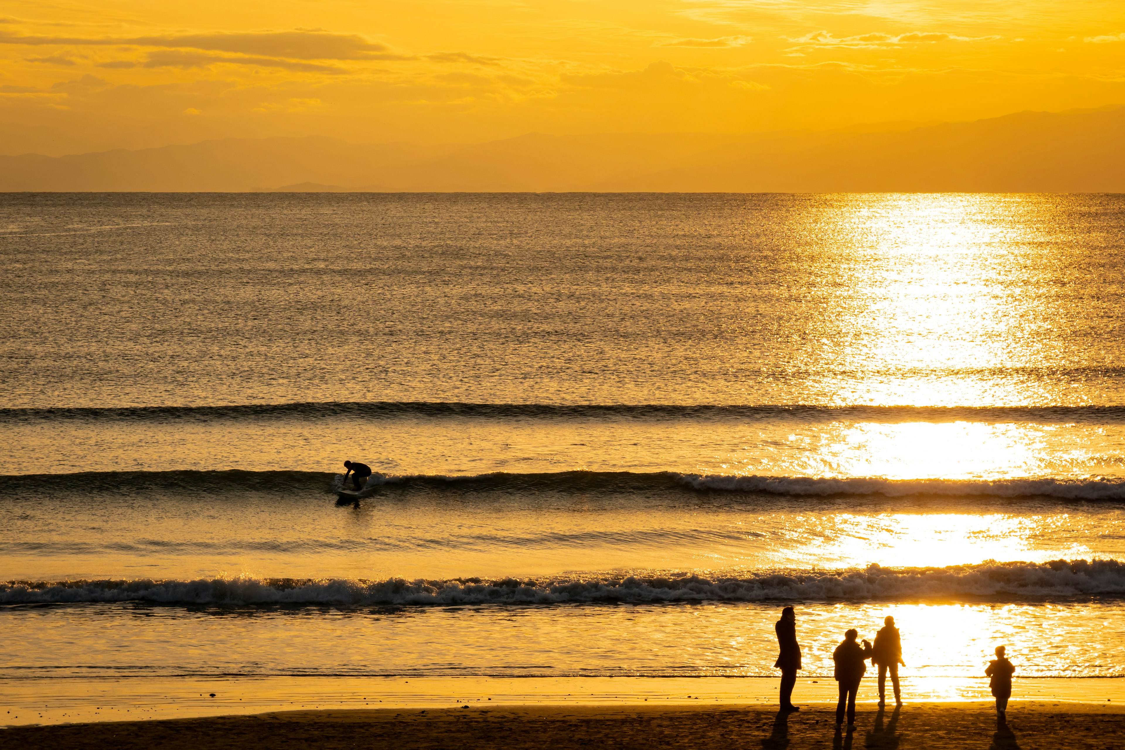 Persone sulla spiaggia al tramonto con un surfista nell'oceano