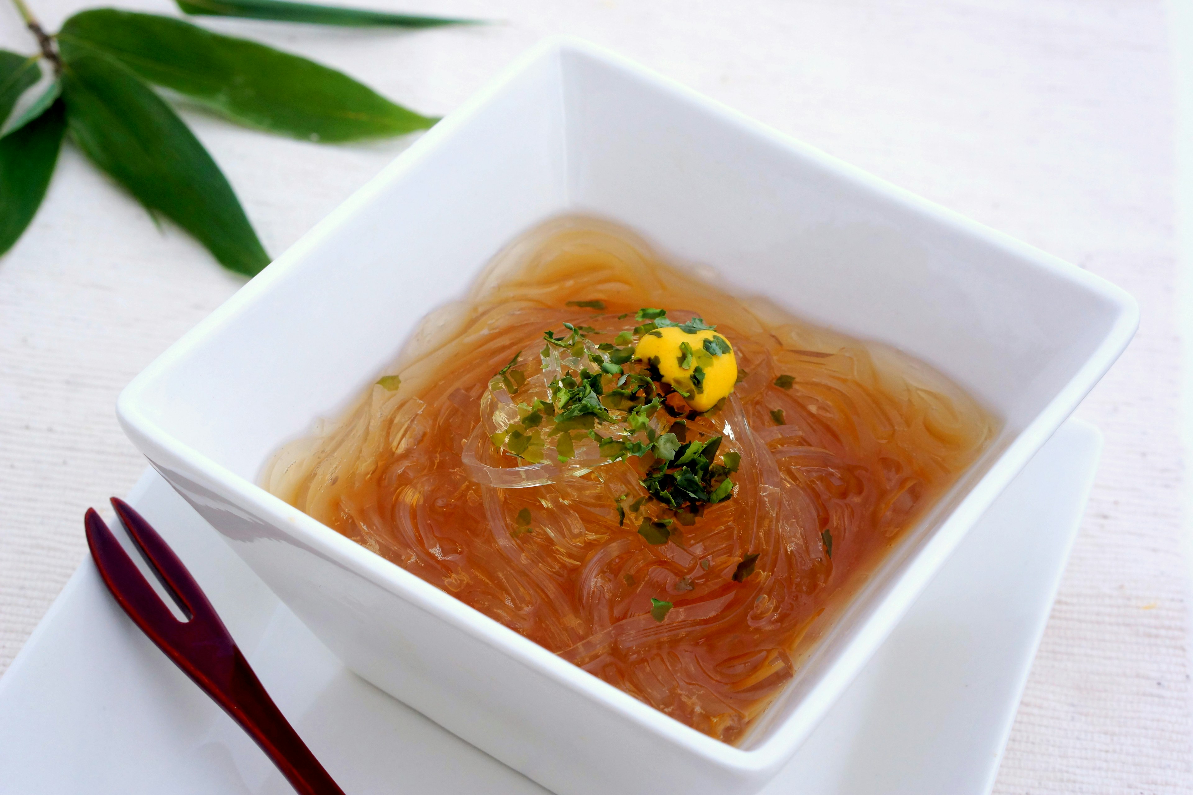 A transparent jelly dessert served in a white bowl topped with a yellow flower garnish surrounded by green leaves