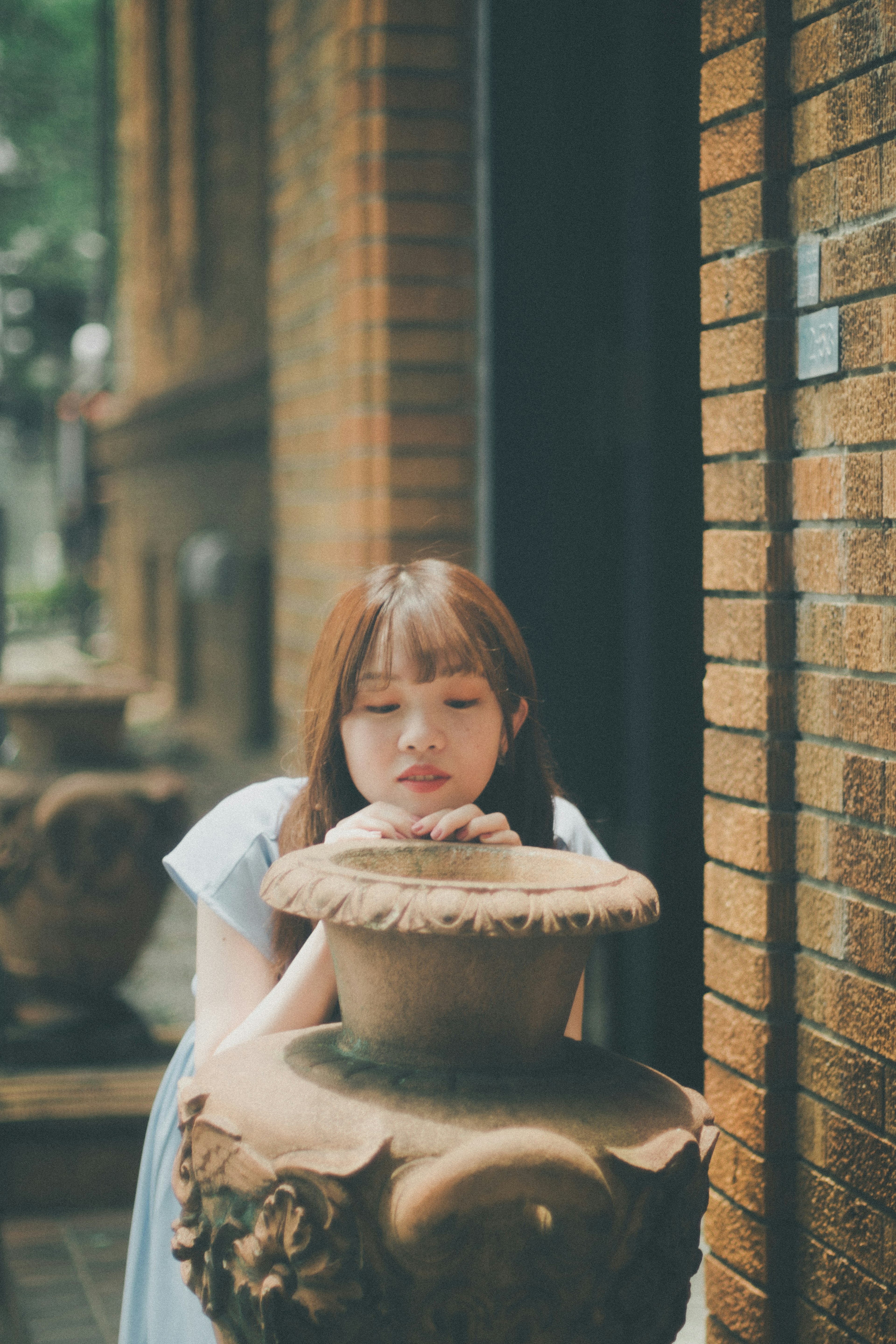 Woman leaning on a ceramic water jar in front of a brown brick wall