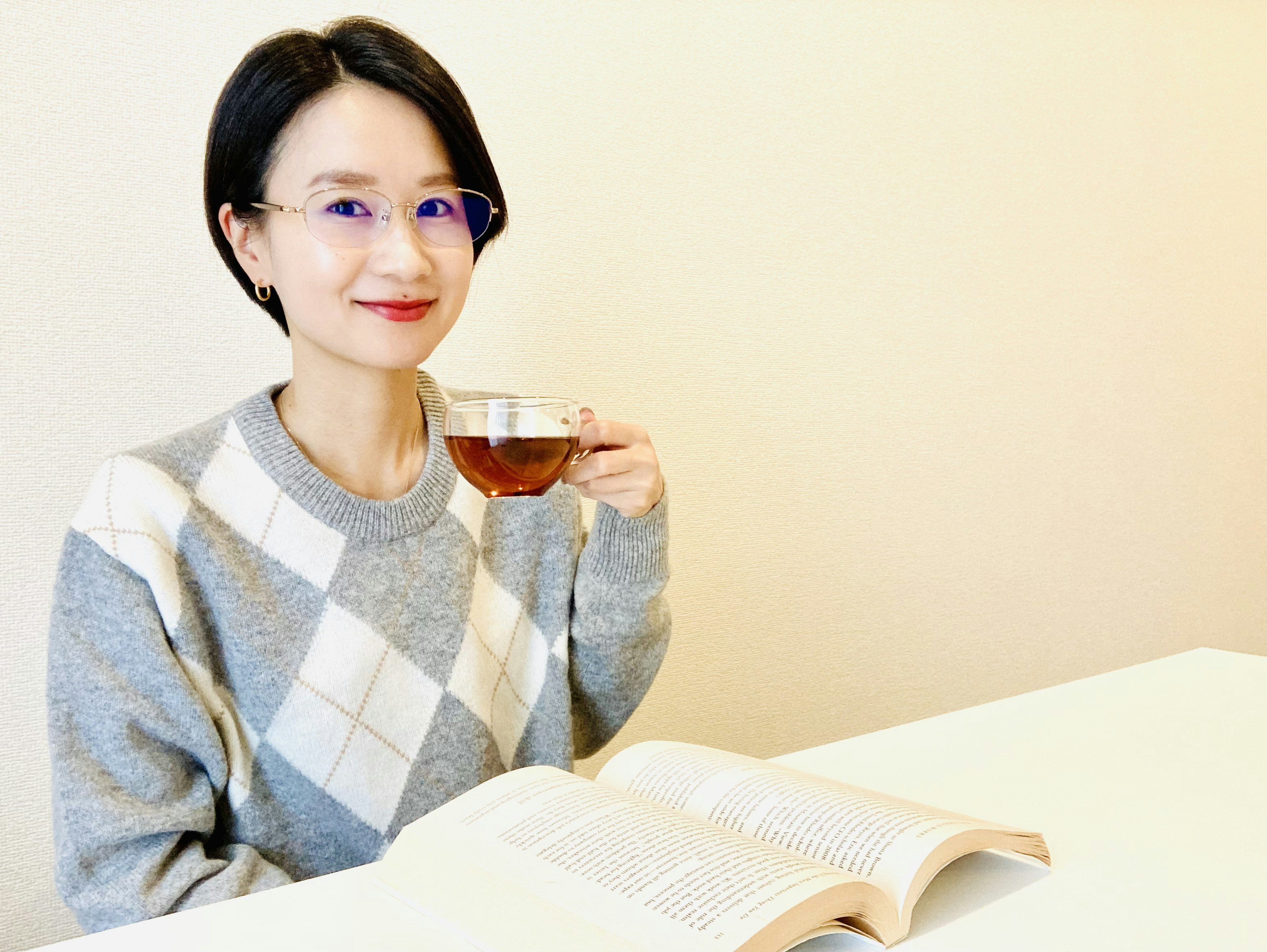 女性手持茶杯坐在桌子旁，桌上有一本打開的書