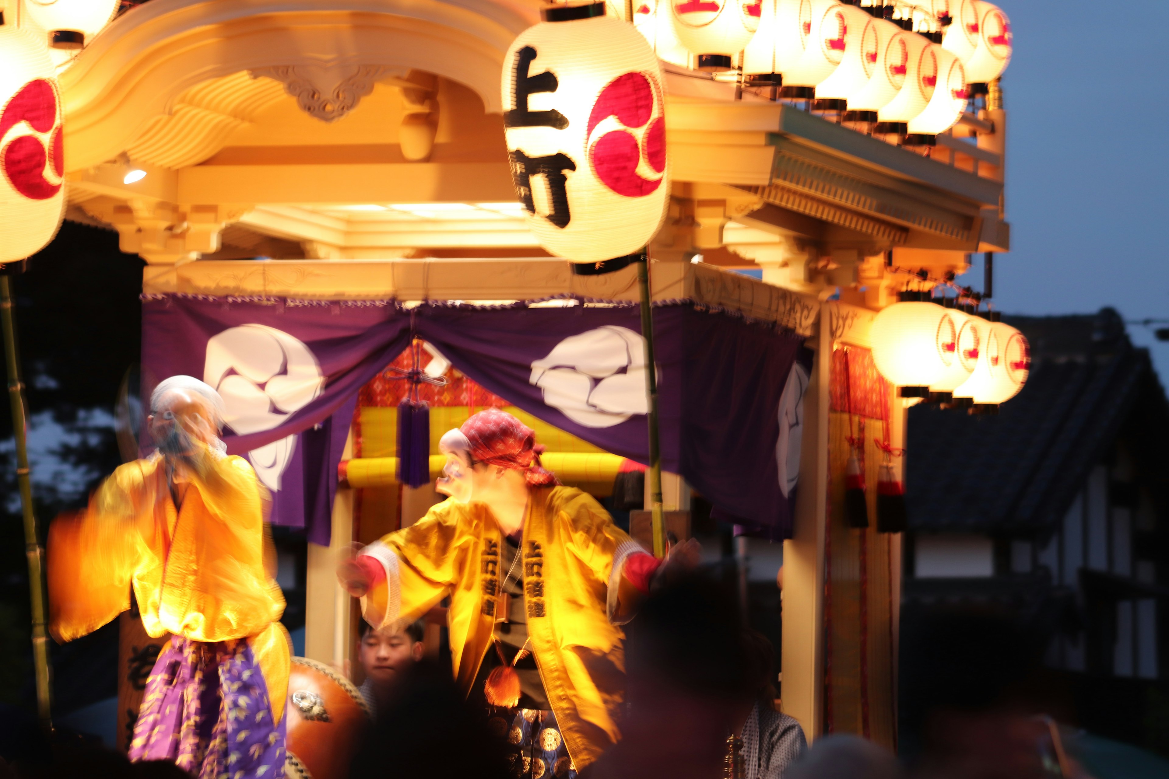 Two performers in traditional costumes dancing at a night festival with lanterns