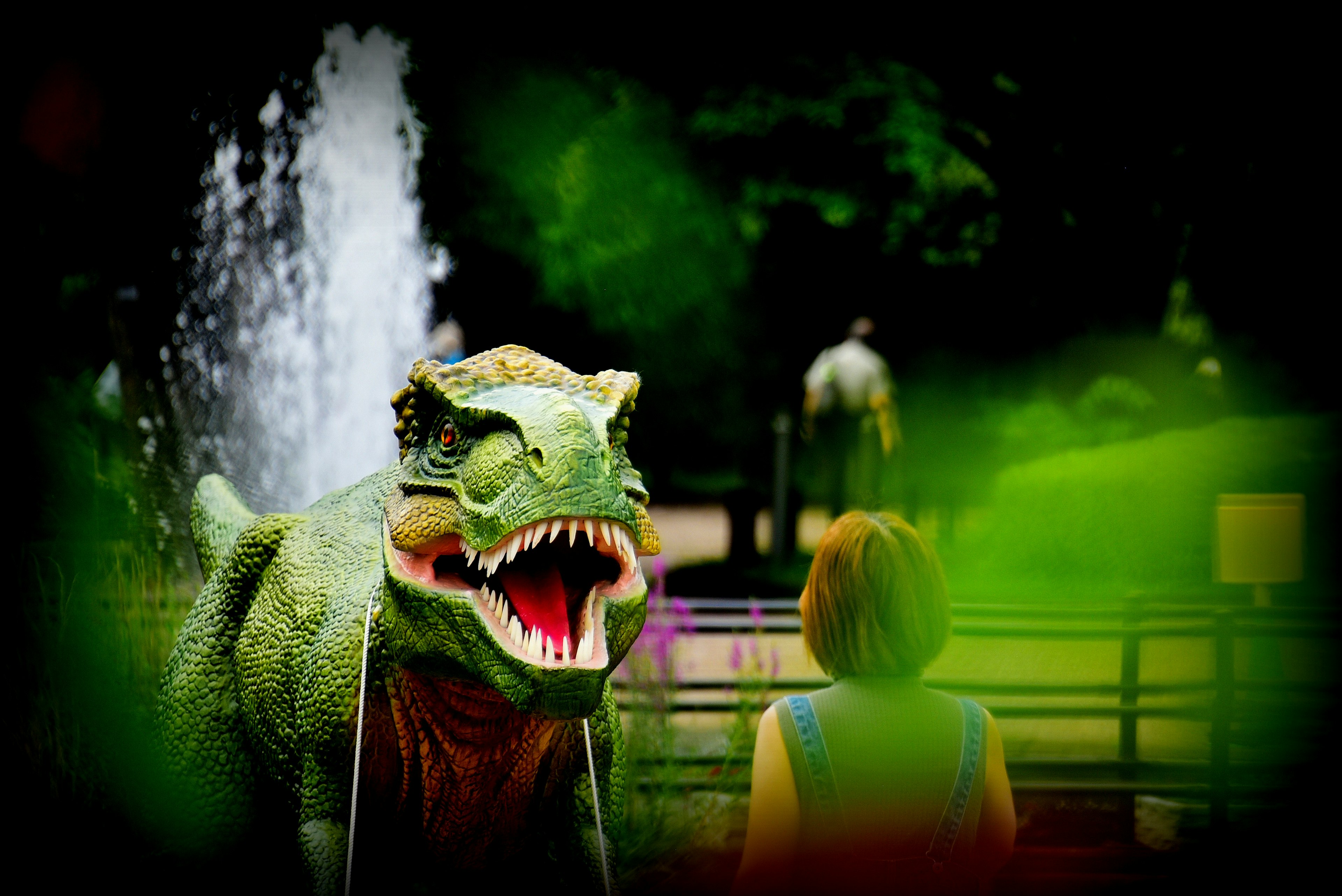 A person in a dinosaur costume near a fountain in a park