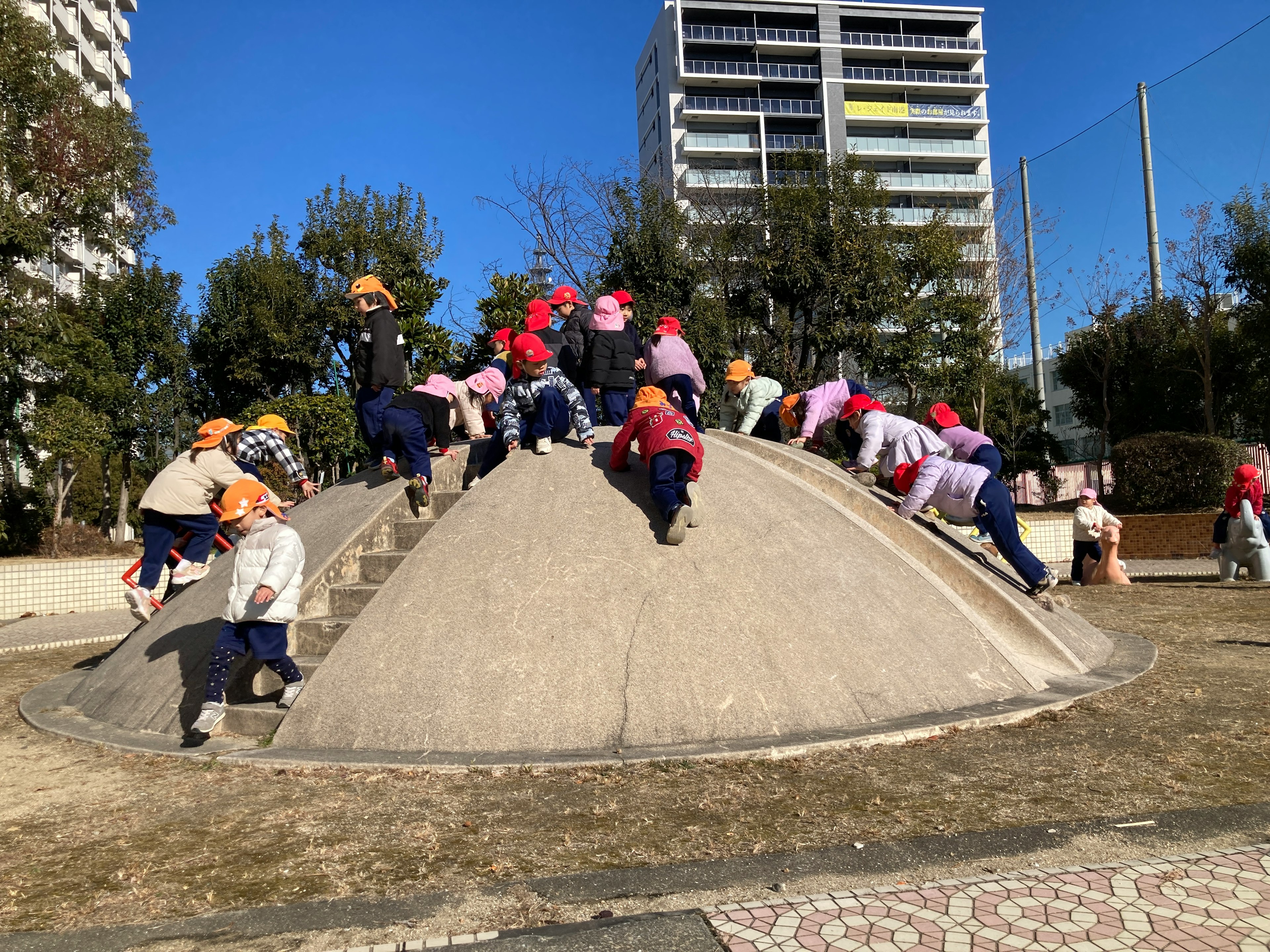 公園で遊ぶ子供たちが滑り台のようなコンクリートの丘を登っている