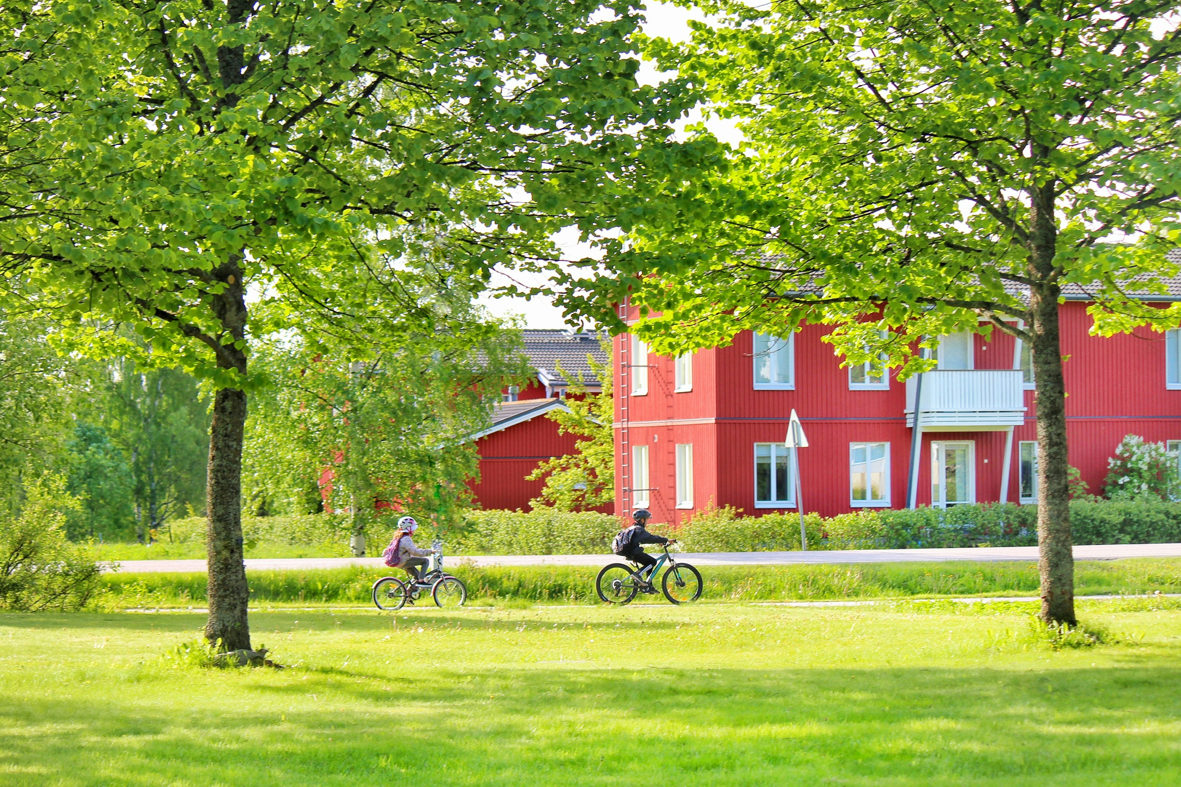 A red house surrounded by green trees with people riding bicycles