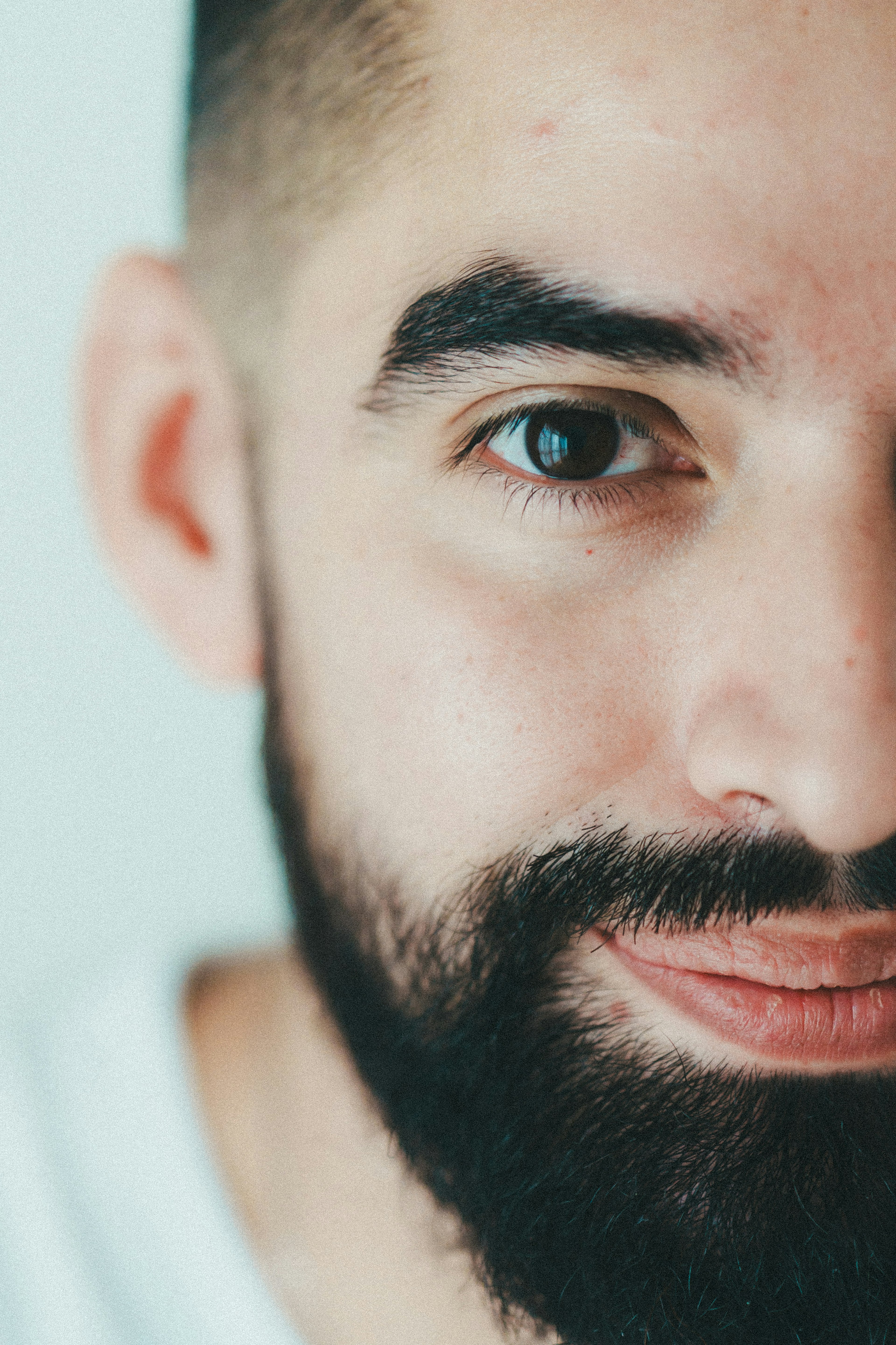 Close-up of a man's face with a smiling expression featuring a beard and prominent eyebrows