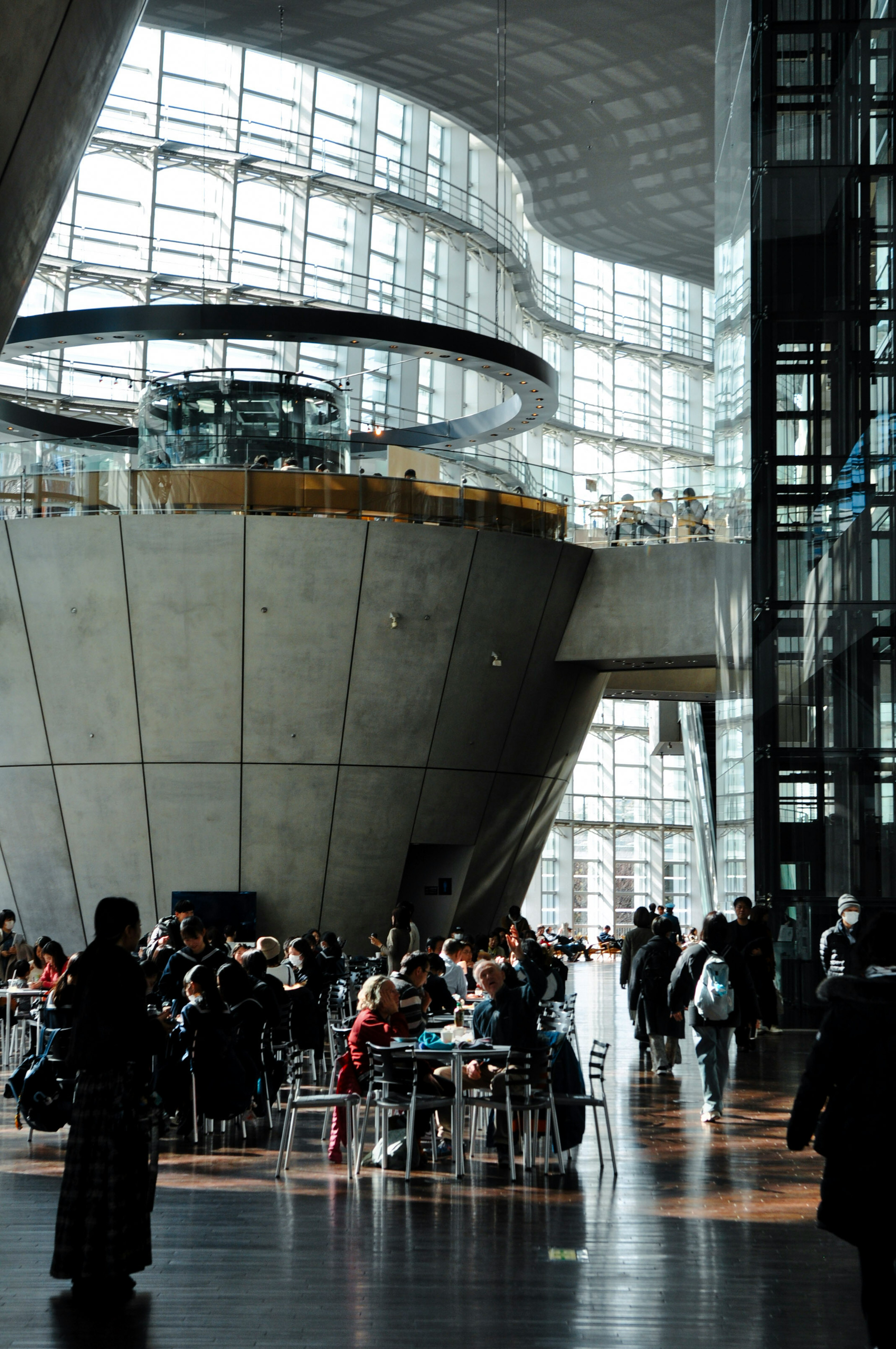 Interior of a modern architectural space with many people gathered large windows allowing natural light