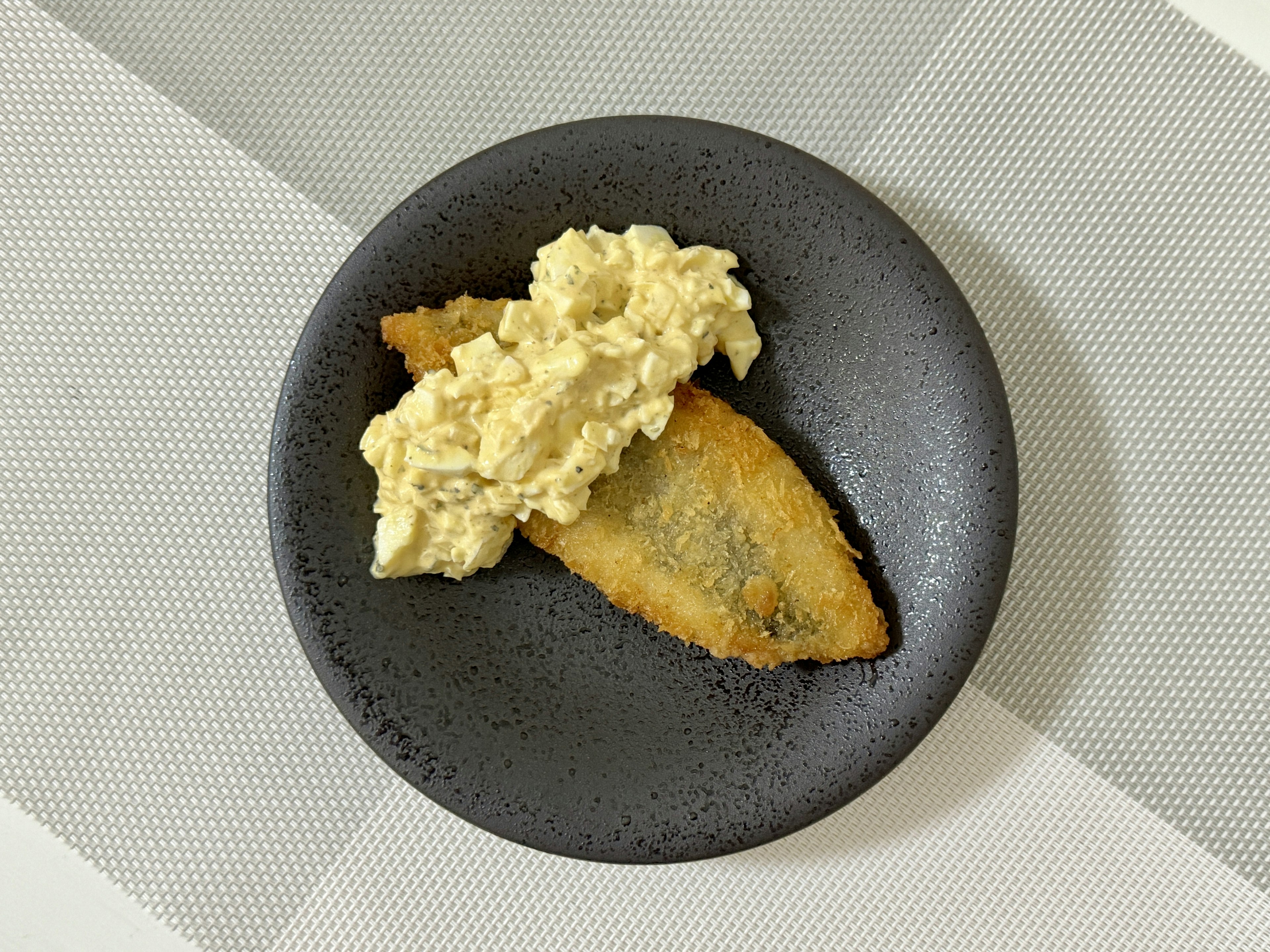 Fried fish with creamy egg salad on a black plate