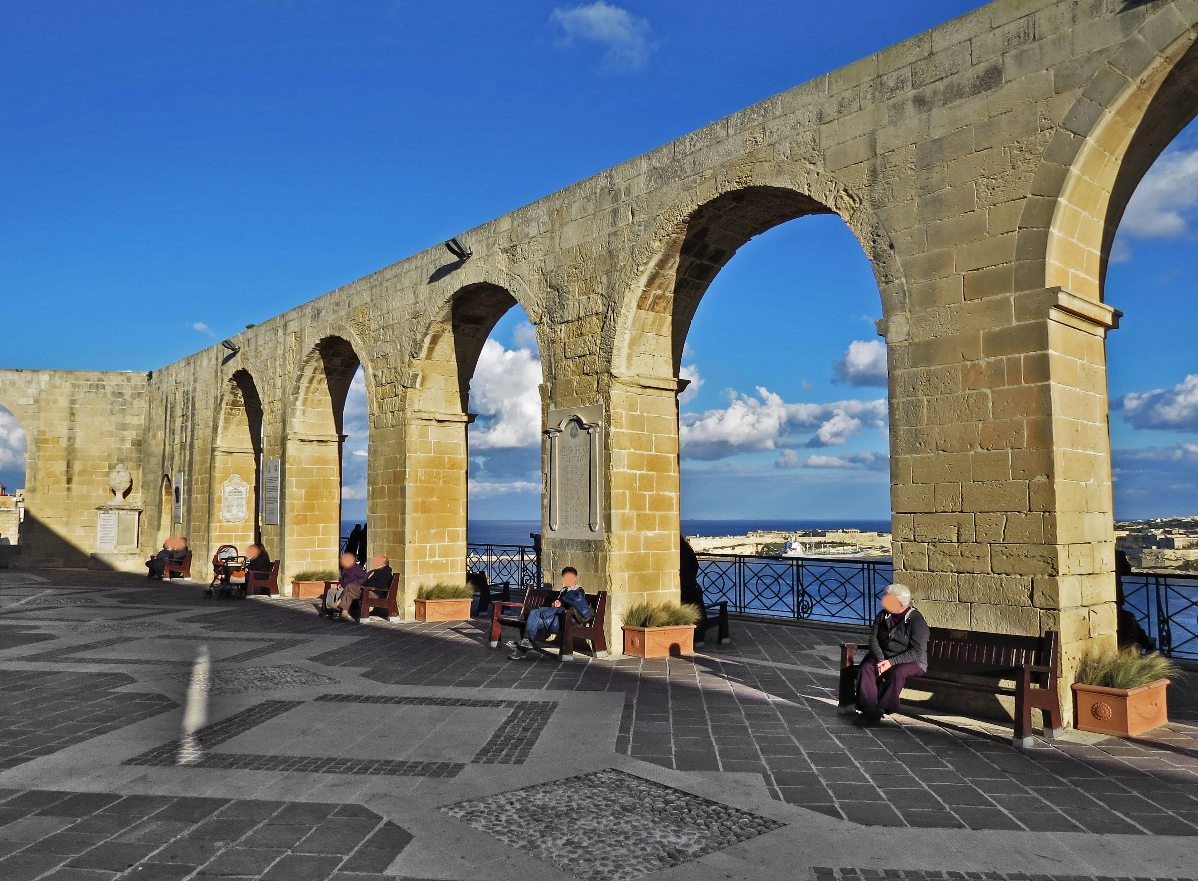 Vista sul mare con archi di pietra e panchine sotto un cielo azzurro